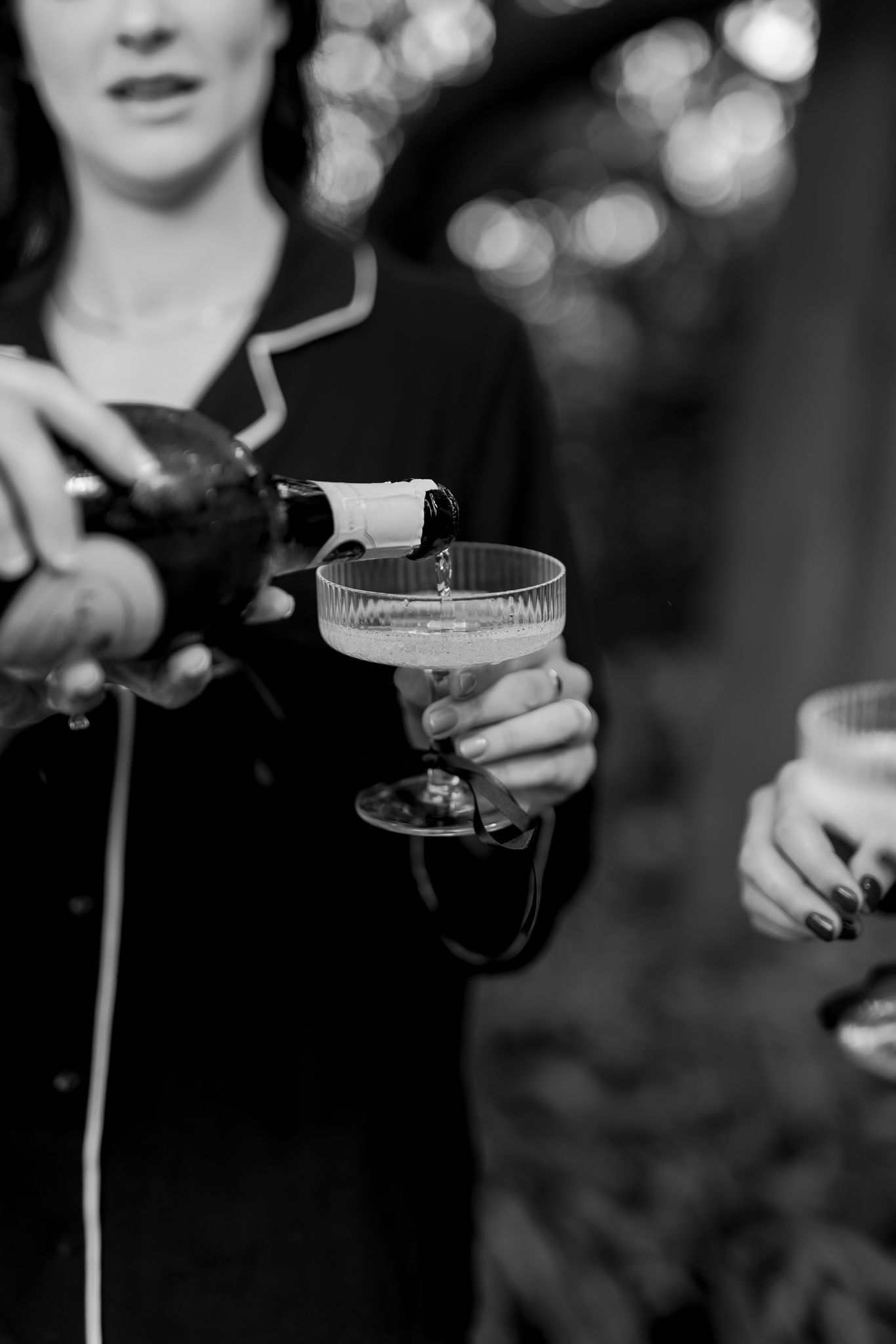 Black and white image of person pouring champagne into vintage coupe glass.