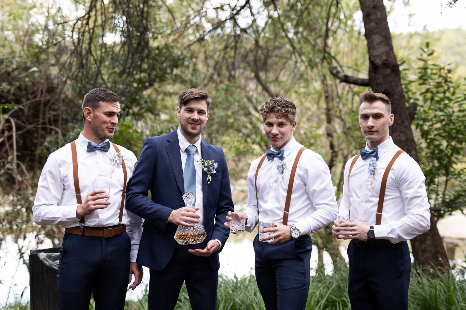 Groomsmen in matching navy and white attire holding drinks outdoors.