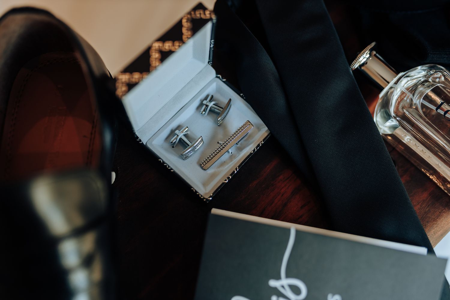 Wedding accessories featuring silver cufflinks and perfume bottle on dark wood surface.