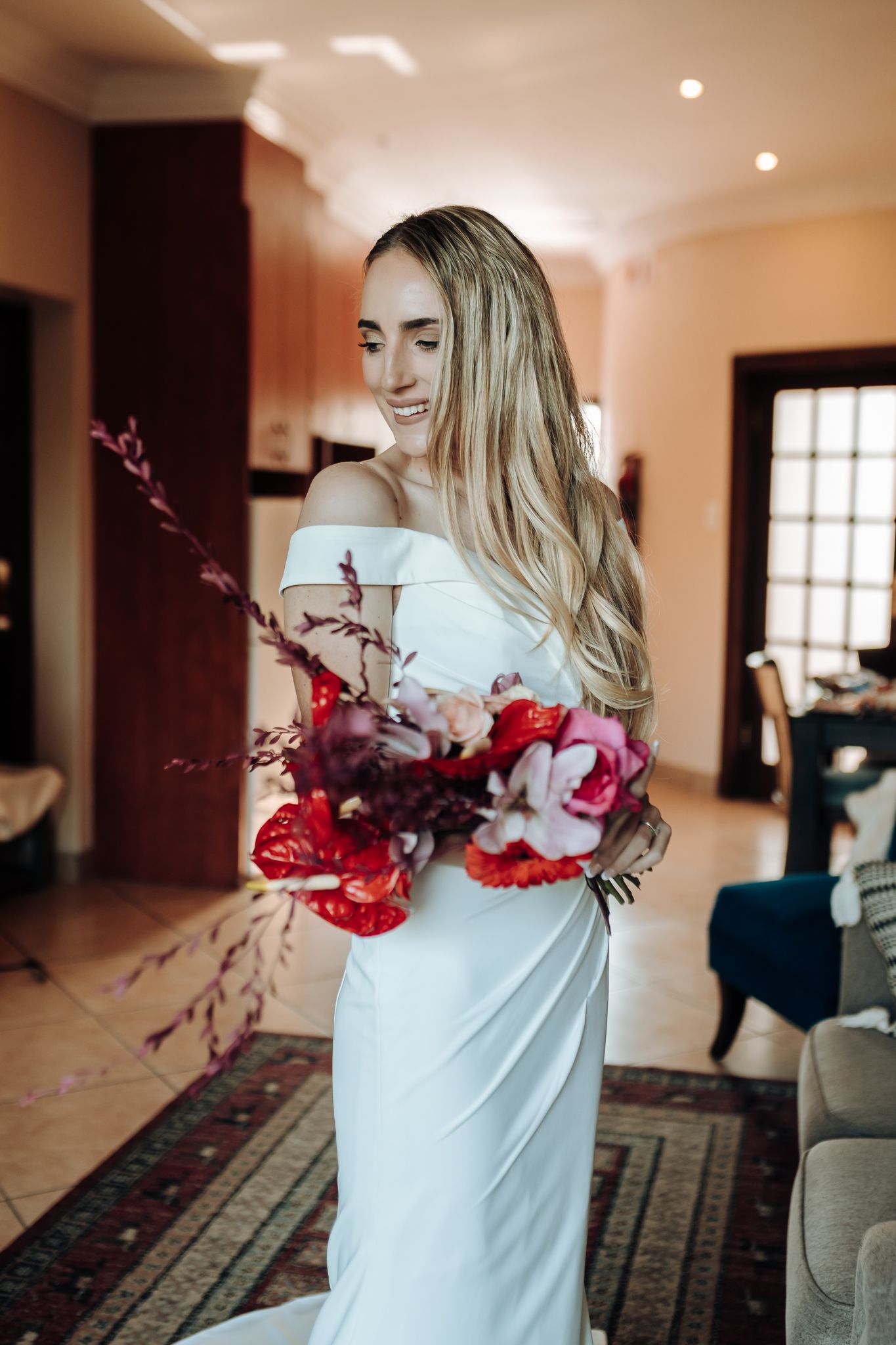 Side profile of elegant wedding dress with dramatic red floral bouquet.