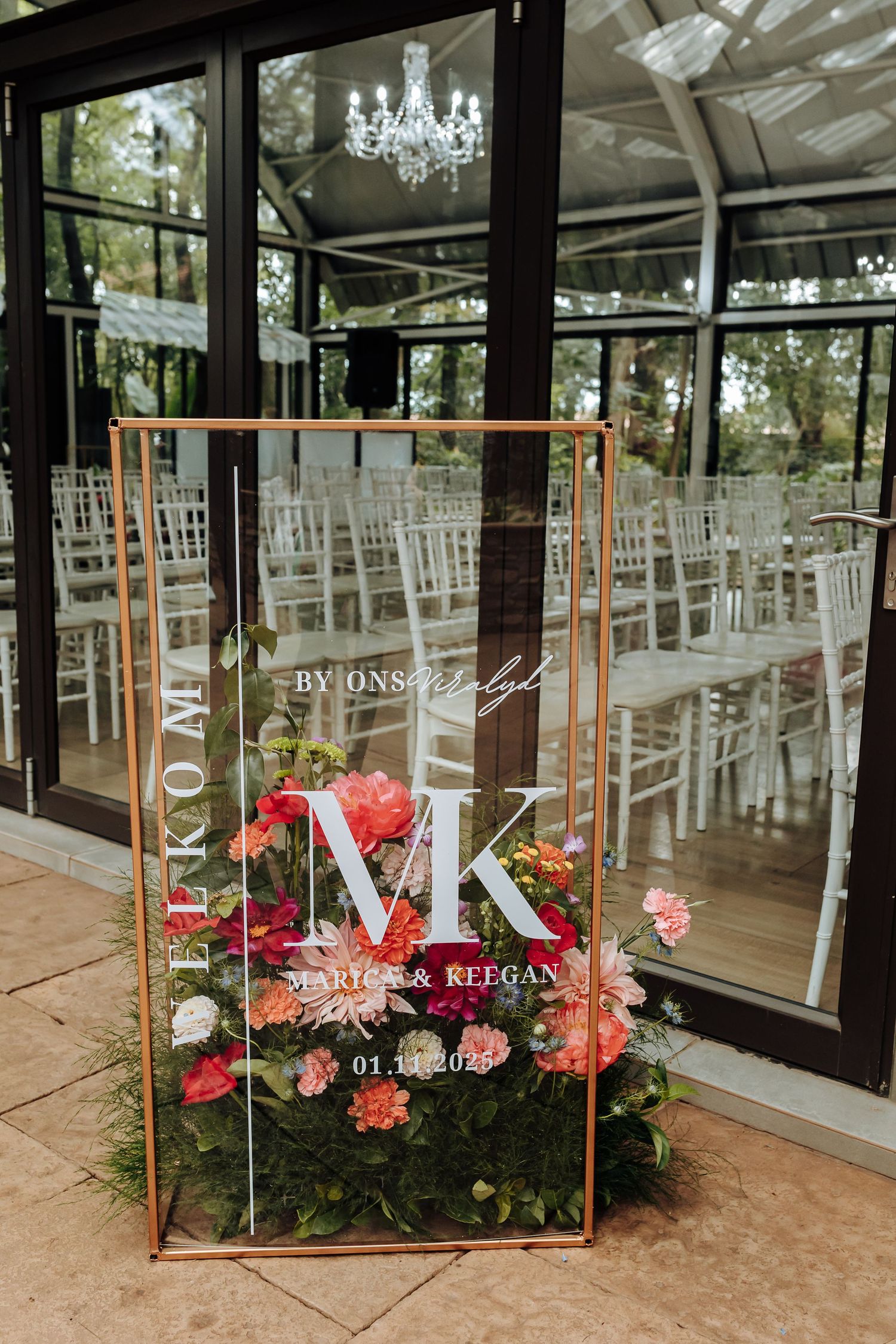 Elegant wedding welcome sign with monogram MK displayed in copper frame with pink and coral floral arrangements.