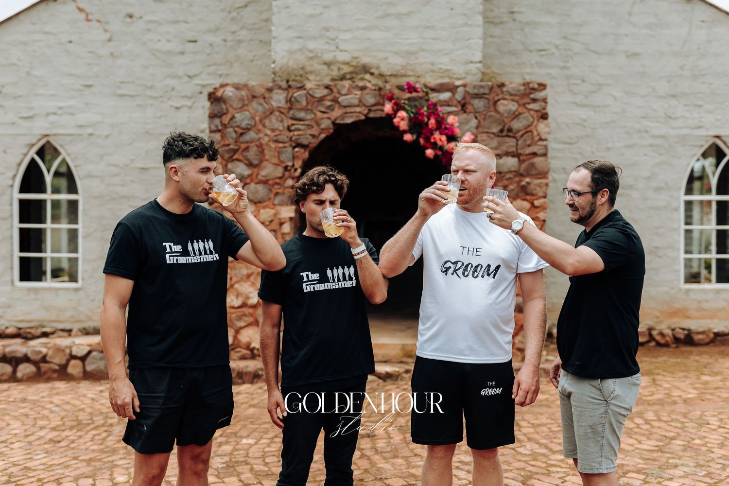 A group in matching black and white outfits stands together in front of a rustic brick wall.