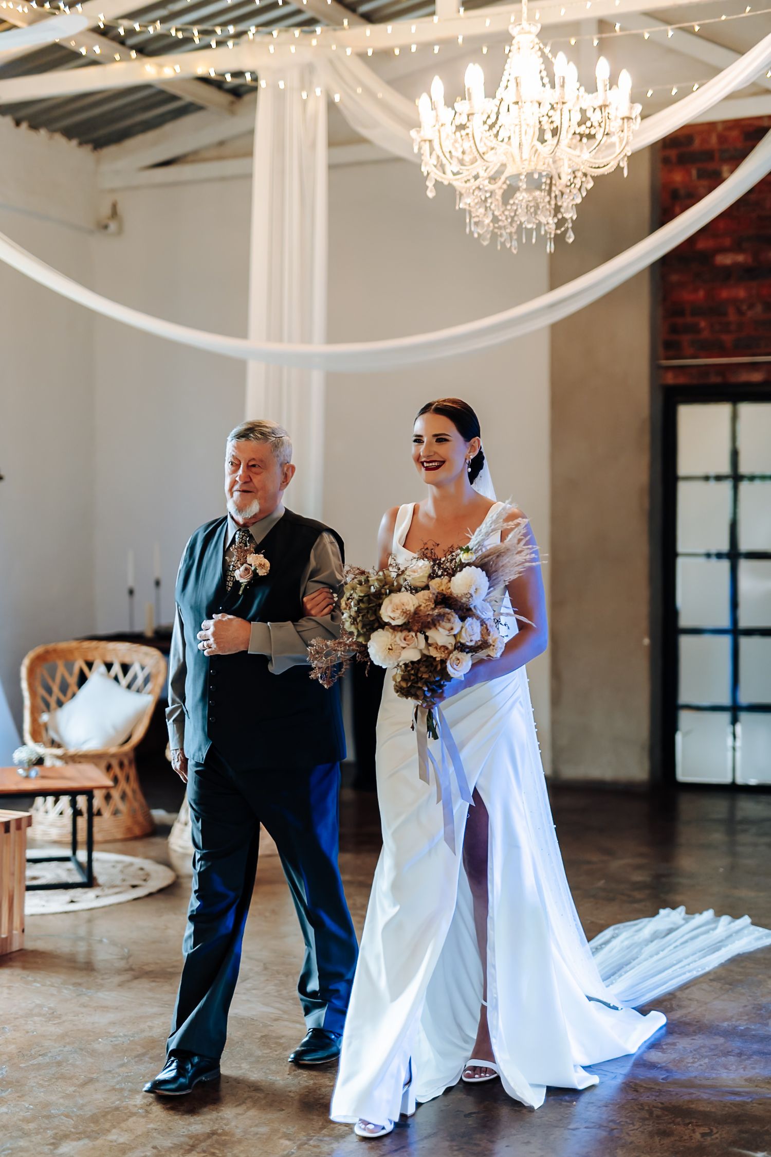 A couple shares a joyful dance moment in an elegant venue with chandeliers and natural light streaming through windows.
