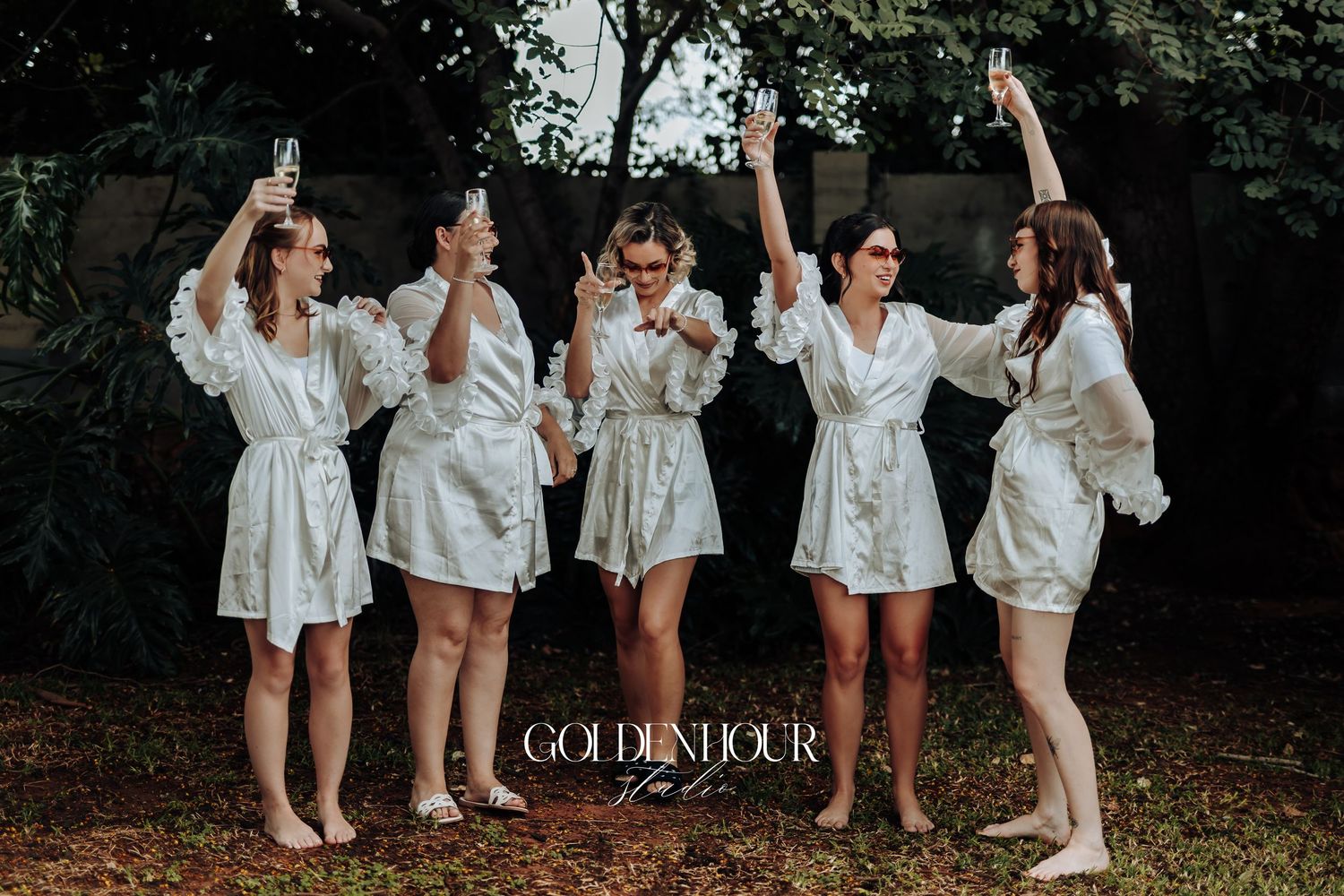 Group of wedding party members in white robes celebrating outdoors.