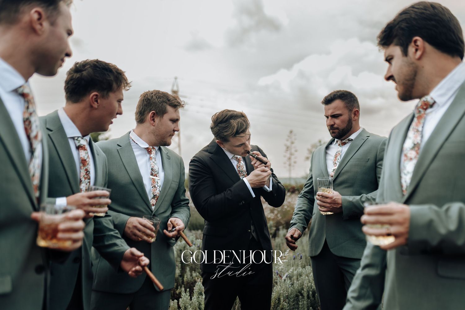 Groomsmen in sage green suits sharing drinks together outdoors.