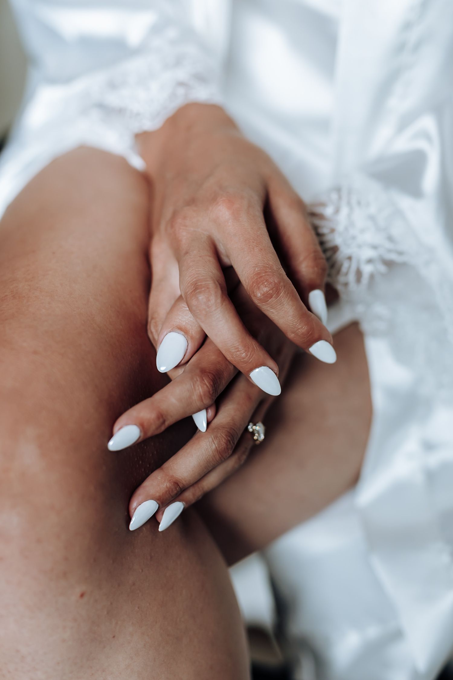 Close-up sequence of hands with white manicured nails wearing an engagement ring against white fabric background.