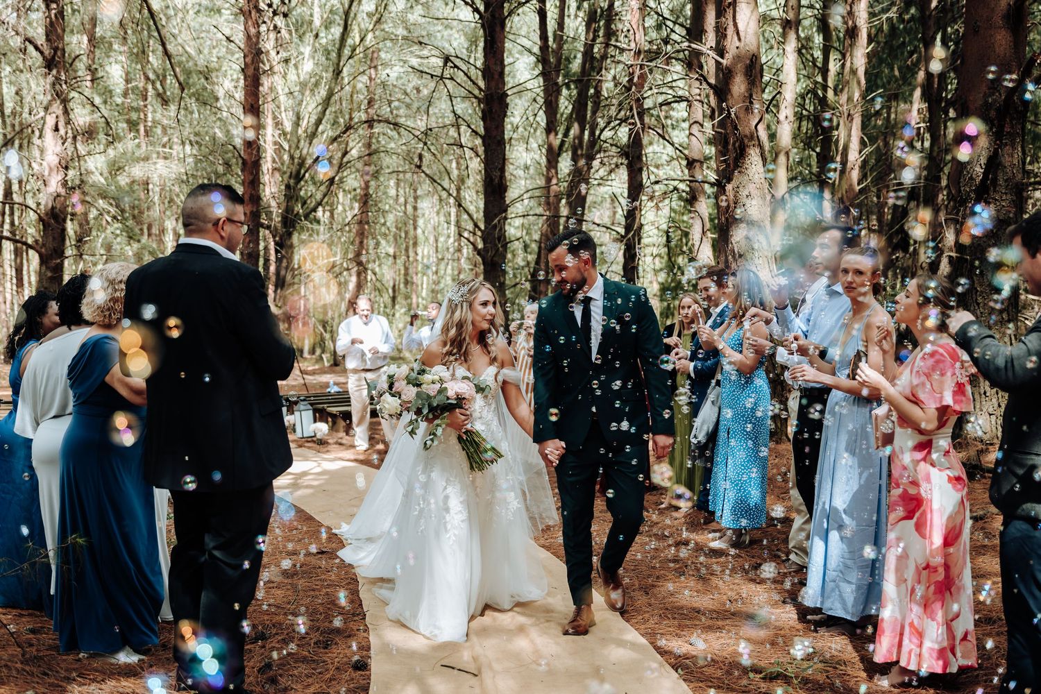 Wedding guests celebrate with confetti in a serene forest setting during an outdoor ceremony.