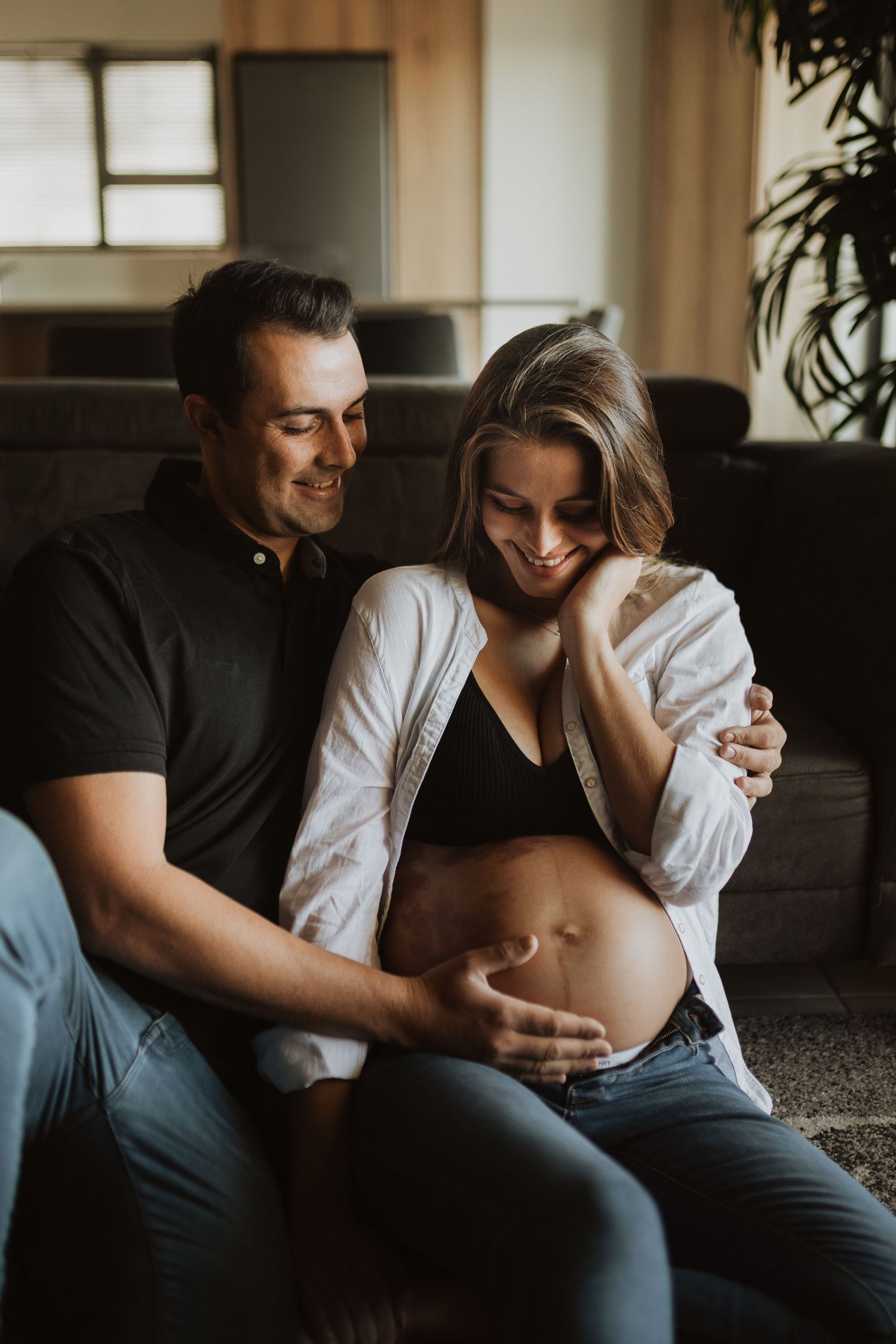 Intimate couple sharing tender moments in moody lighting on a couch with focus on expecting mother.