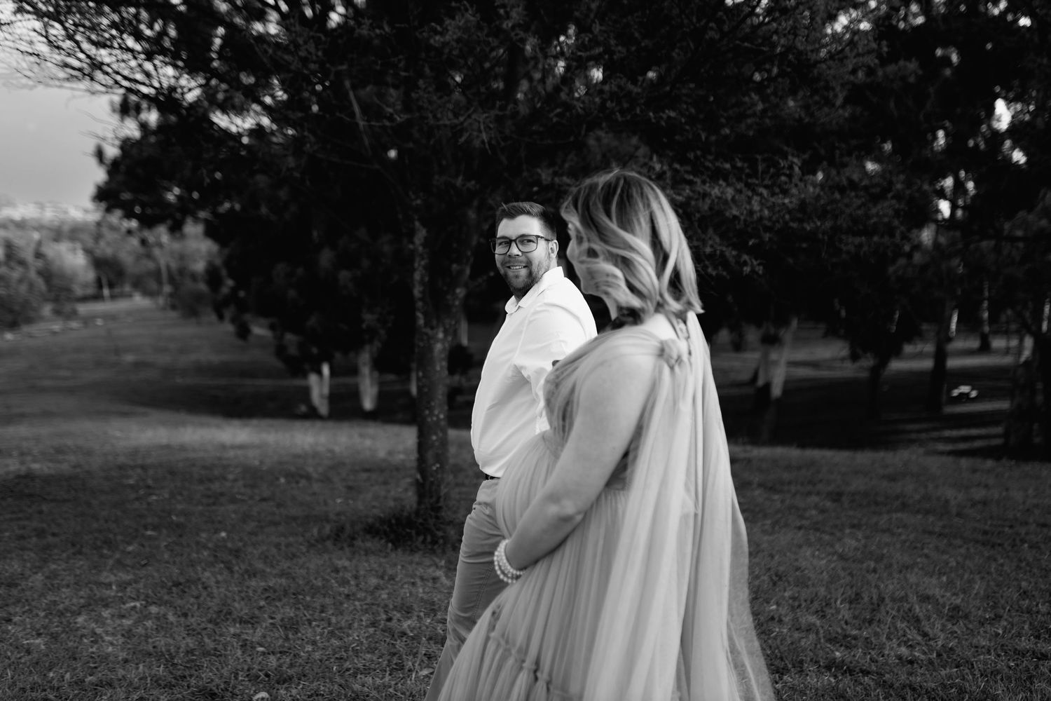 Black and white outdoor wedding photo showing a couple standing in a serene orchard setting.