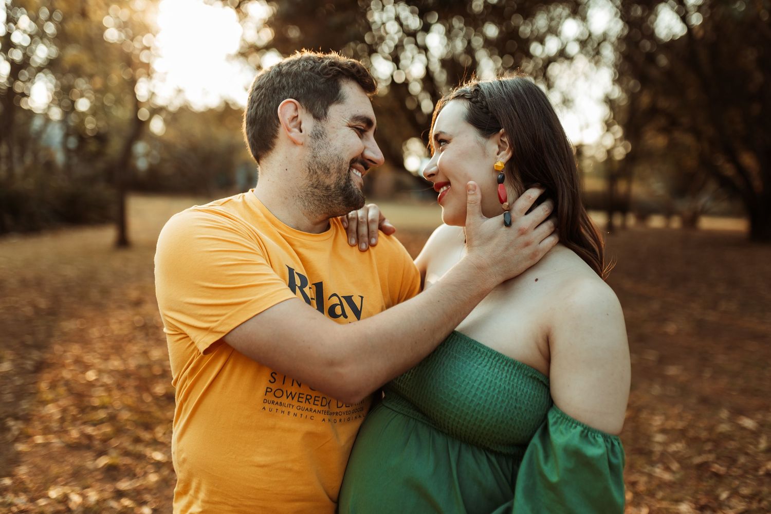 A couple shares a romantic moment together in a fall setting while wearing yellow and green outfits.