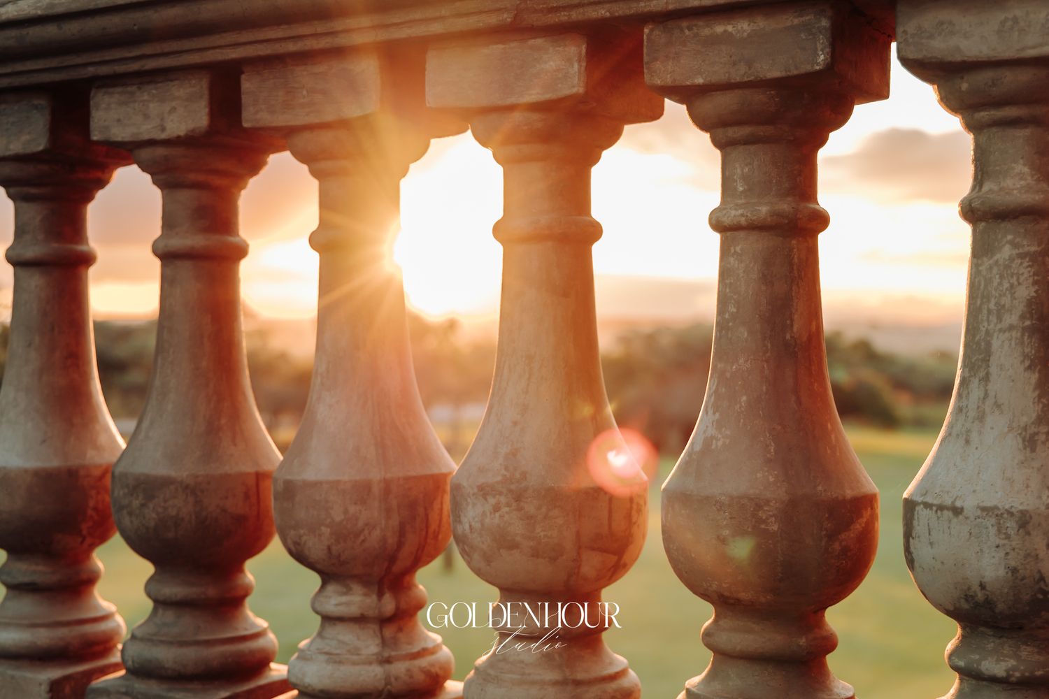 Golden sunset light streaming through ornate stone balustrade columns at outdoor wedding venue.