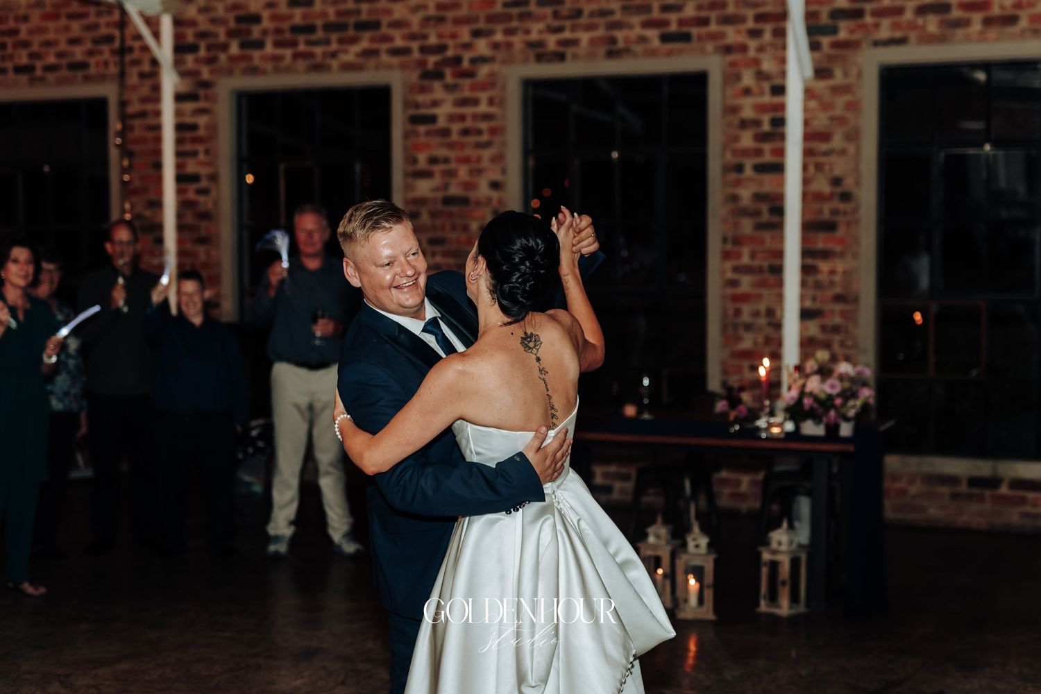 Bride and groom share their first dance in a warmly lit brick-walled wedding reception venue.