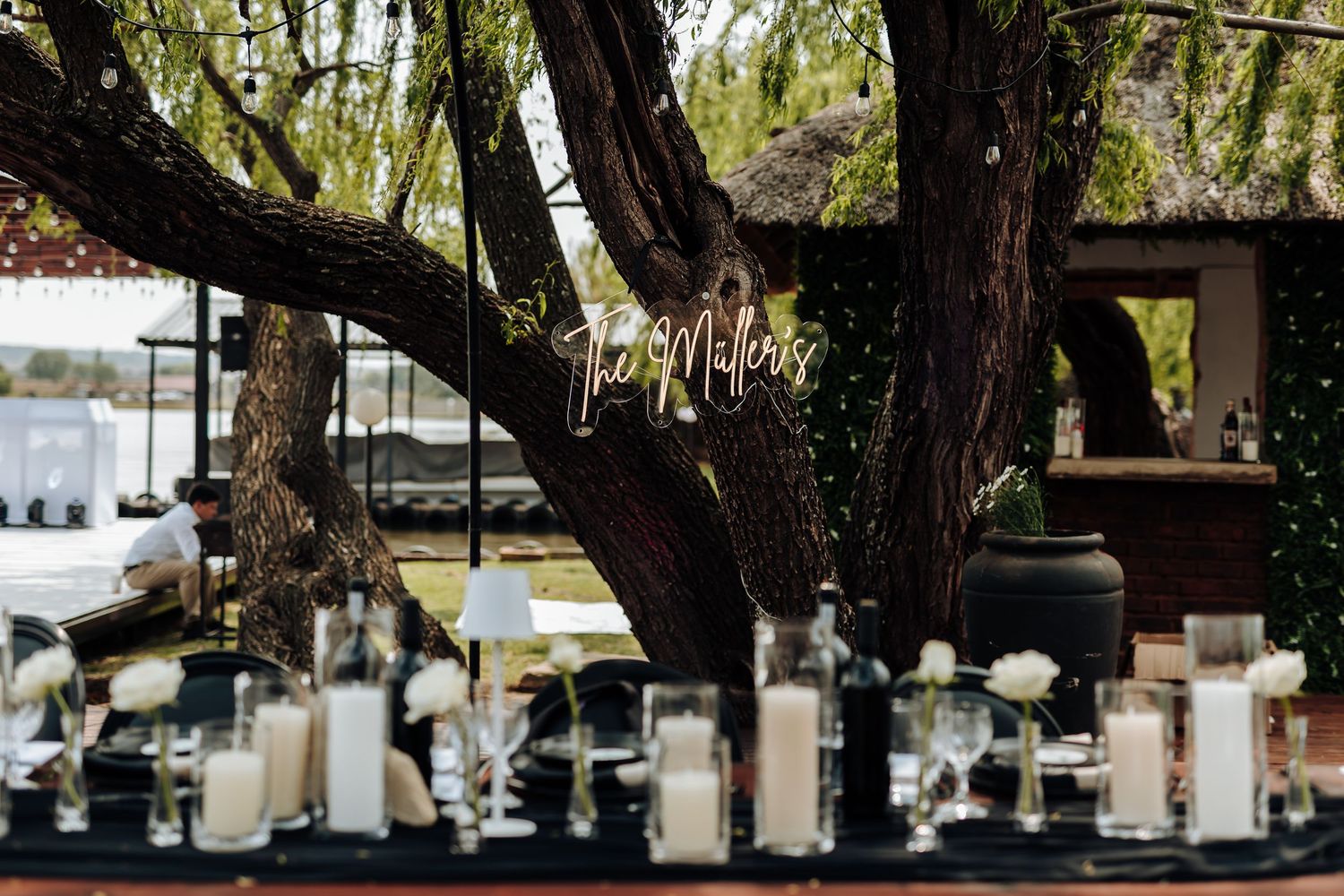 White lanterns and fairy lights hang from tree branches creating a romantic outdoor wedding reception setting.