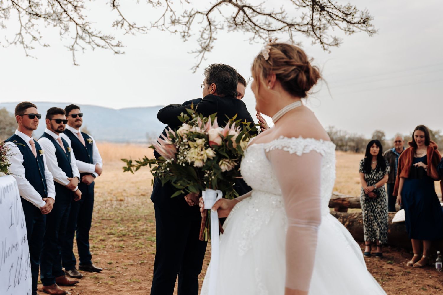 A scenic outdoor wedding ceremony is taking place on a mountain overlook with guests watching in the fall.