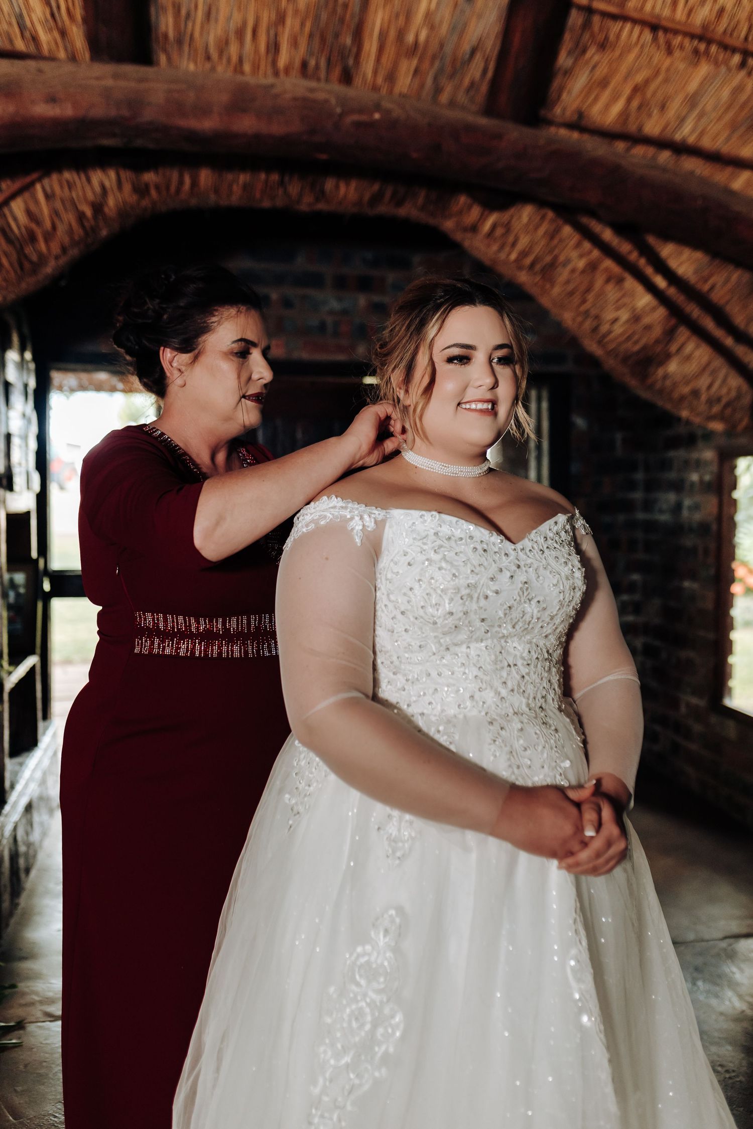 Close up view of a couple embracing in burgundy and white wedding attire under brick archway.