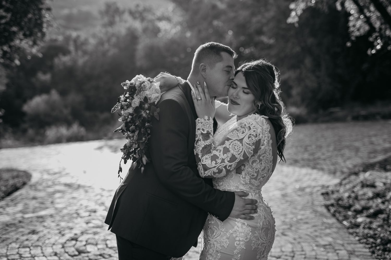Intimate black and white photo of newlyweds sharing tender moment outdoors.