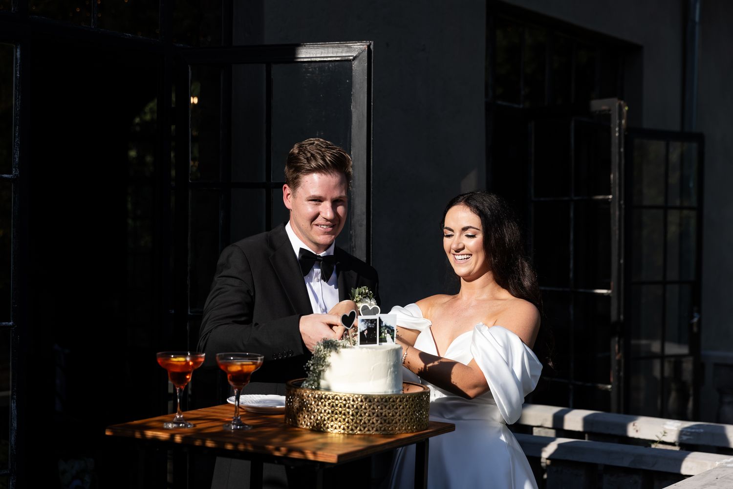 A couple cutting their wedding cake together in a modern venue with natural lighting.