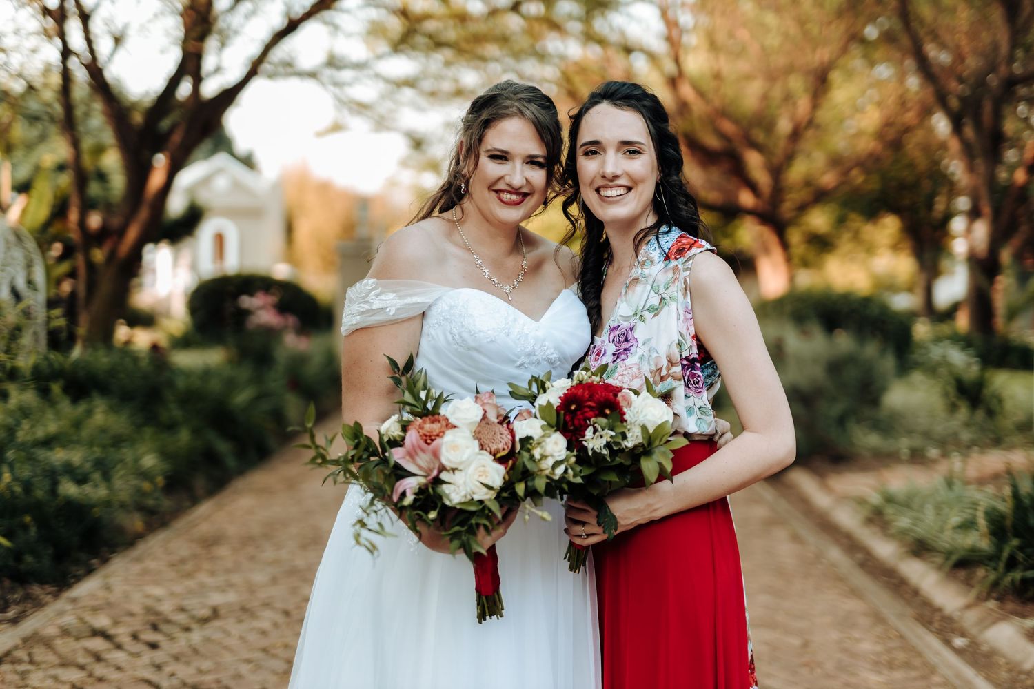 Bridal party members in white and red attire smile while holding matching bouquets.