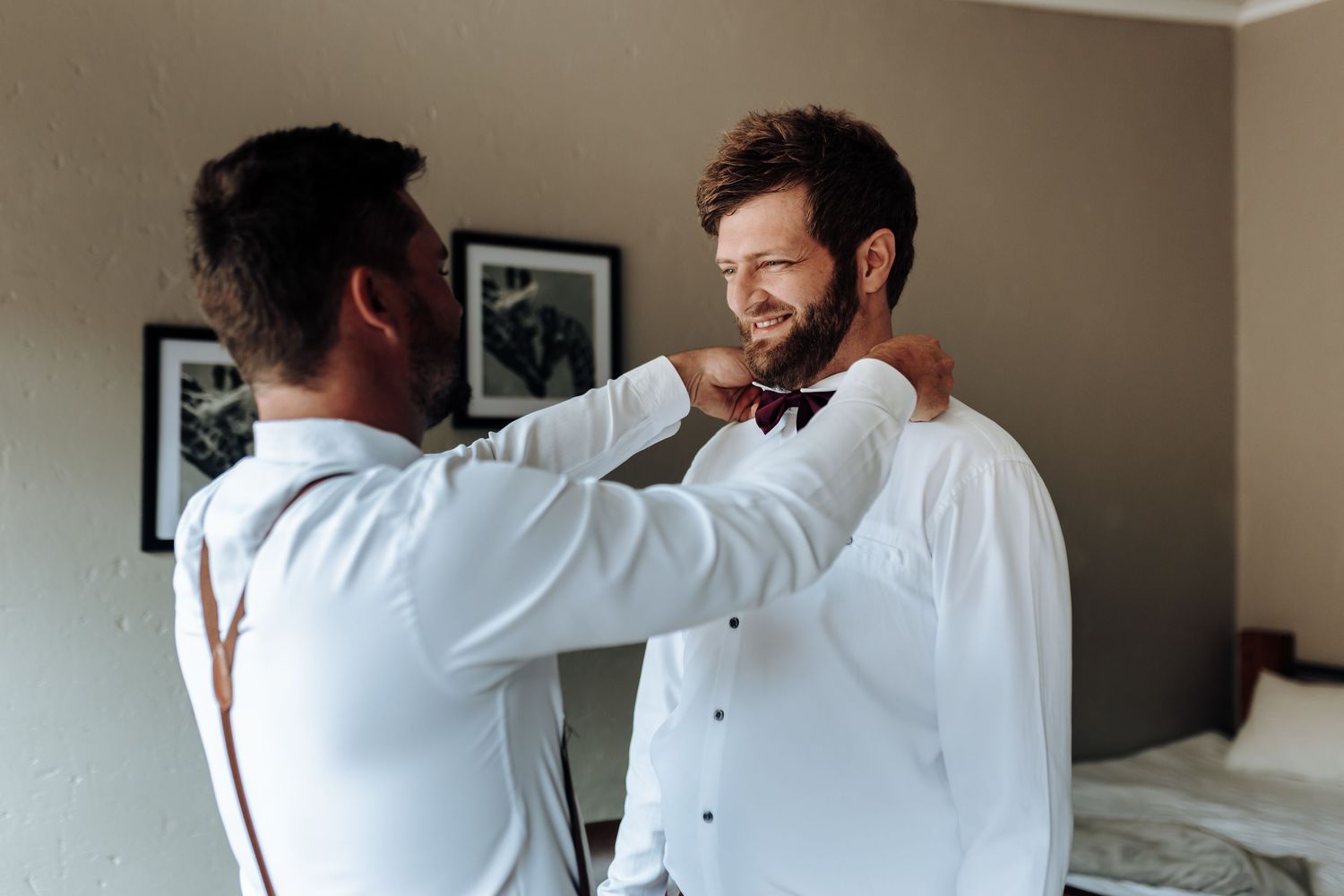 Two people in white dress shirts adjusting formal attire indoors.