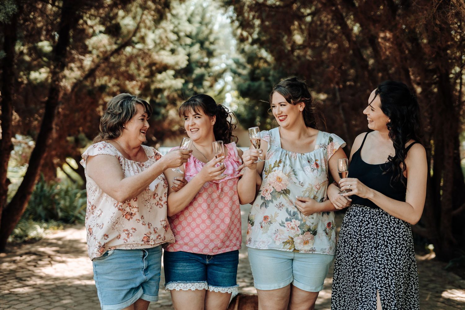 Friends in summer outfits sharing drinks and laughter on a sunny forest path.