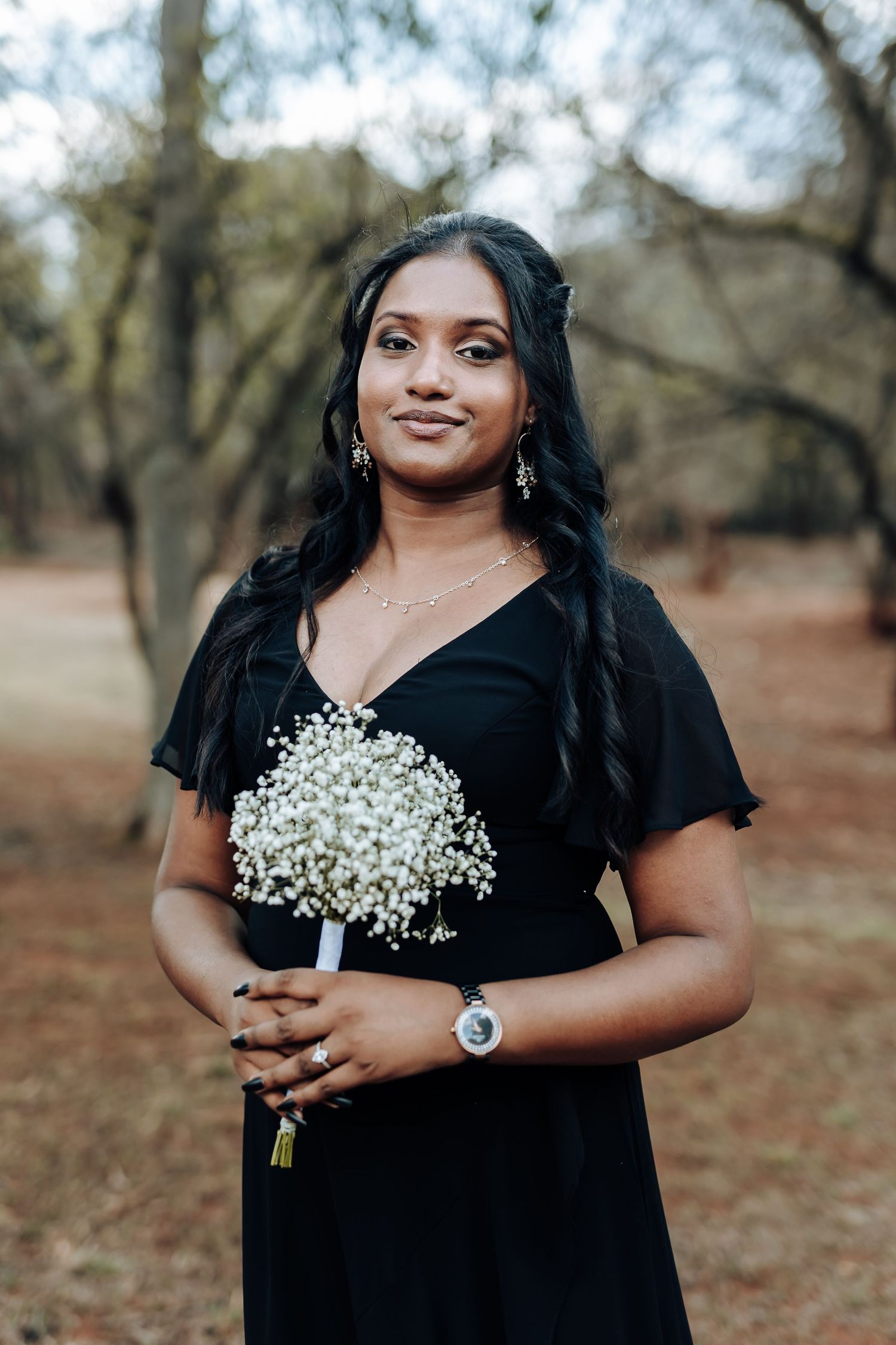 Woman in black formal dress holds baby's breath bouquet in outdoor setting.