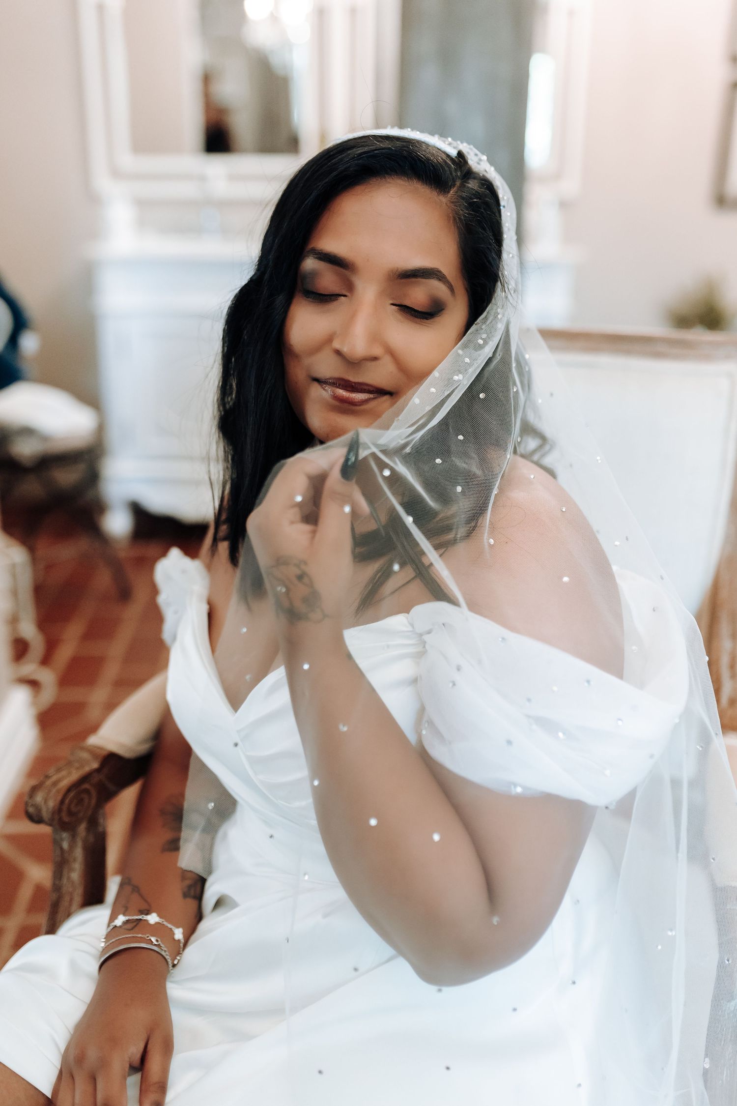 Bride with dark hair wearing sparkly veil and white gown poses with closed eyes.