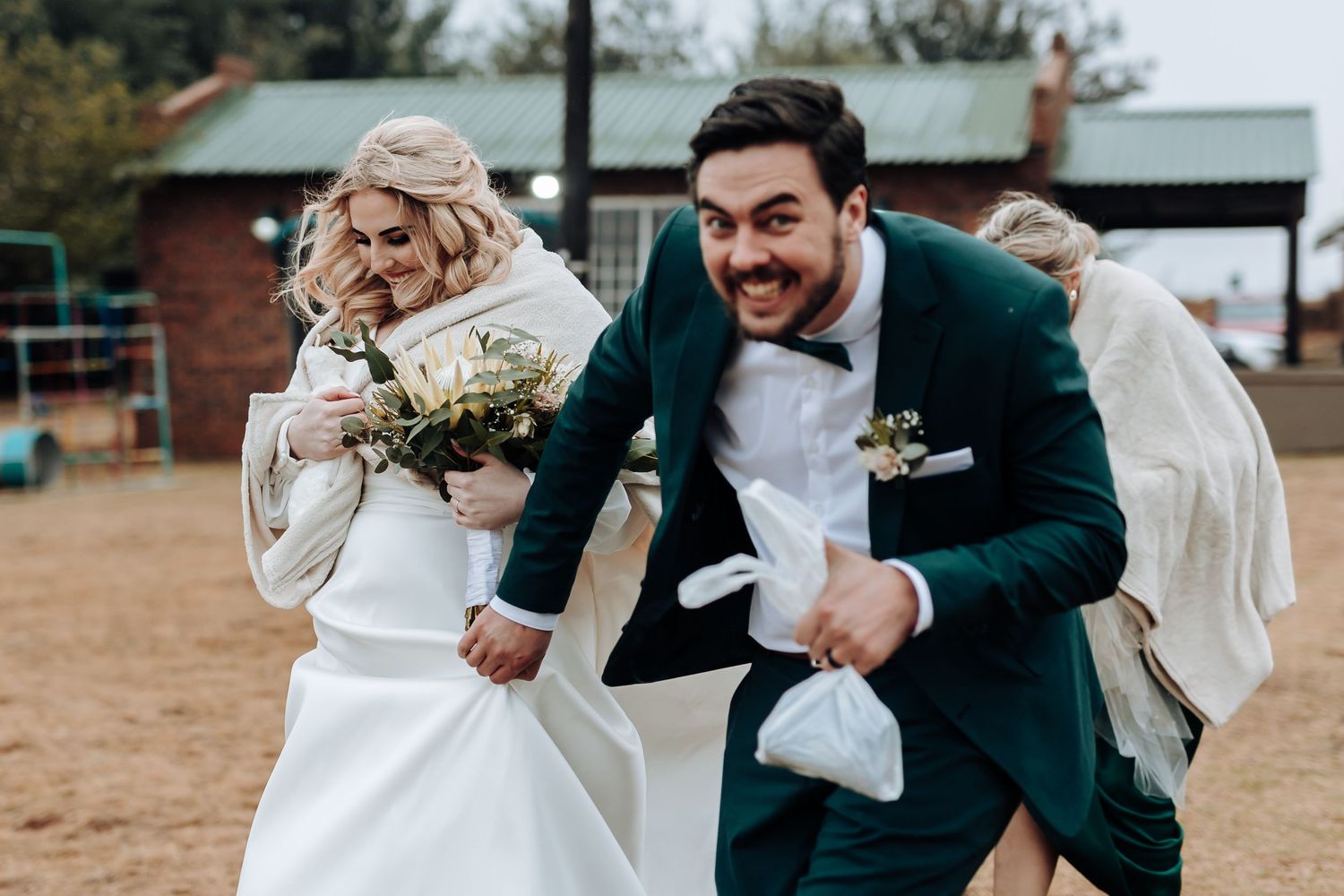 Joyful wedding couple laughs and dances together outdoors in casual celebration.