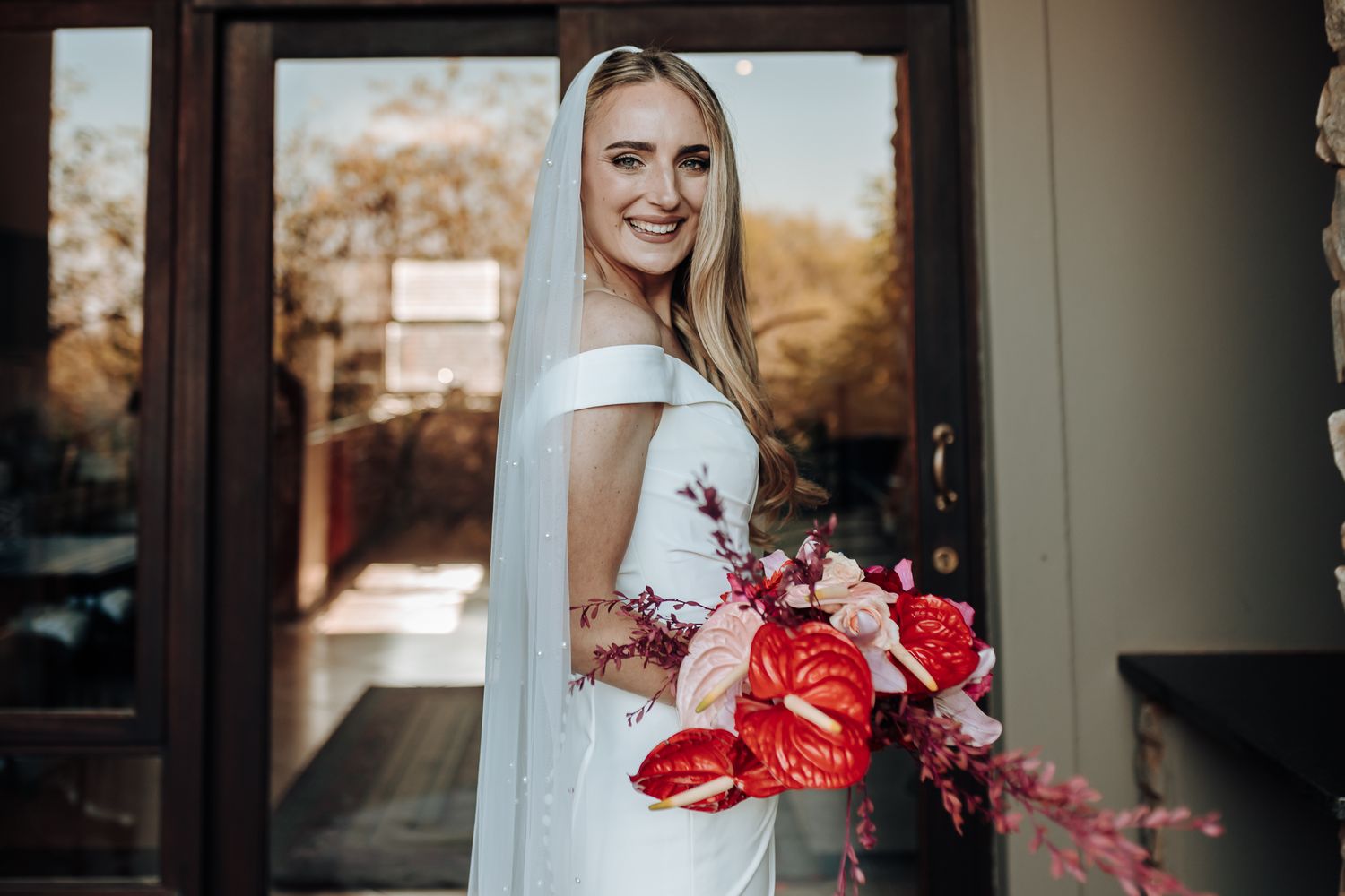Elegant bridal portrait featuring off-shoulder dress and vibrant red floral bouquet.