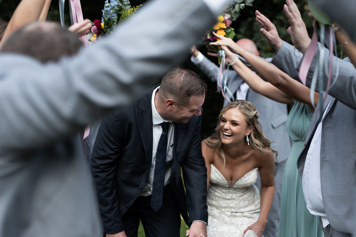 Wedding couple walking through crowd of raised hands during outdoor celebration.
