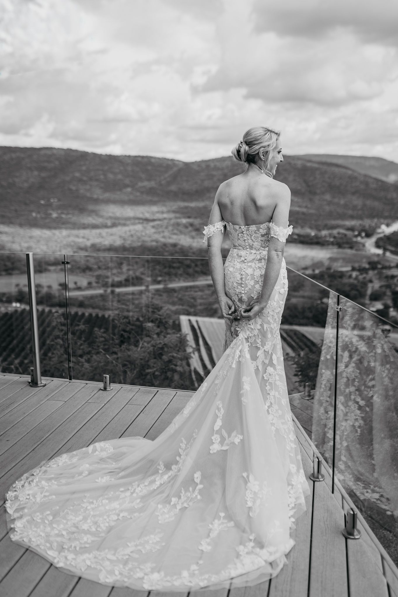 Black and white photo of bride in fitted wedding dress looking out over mountain landscape.
