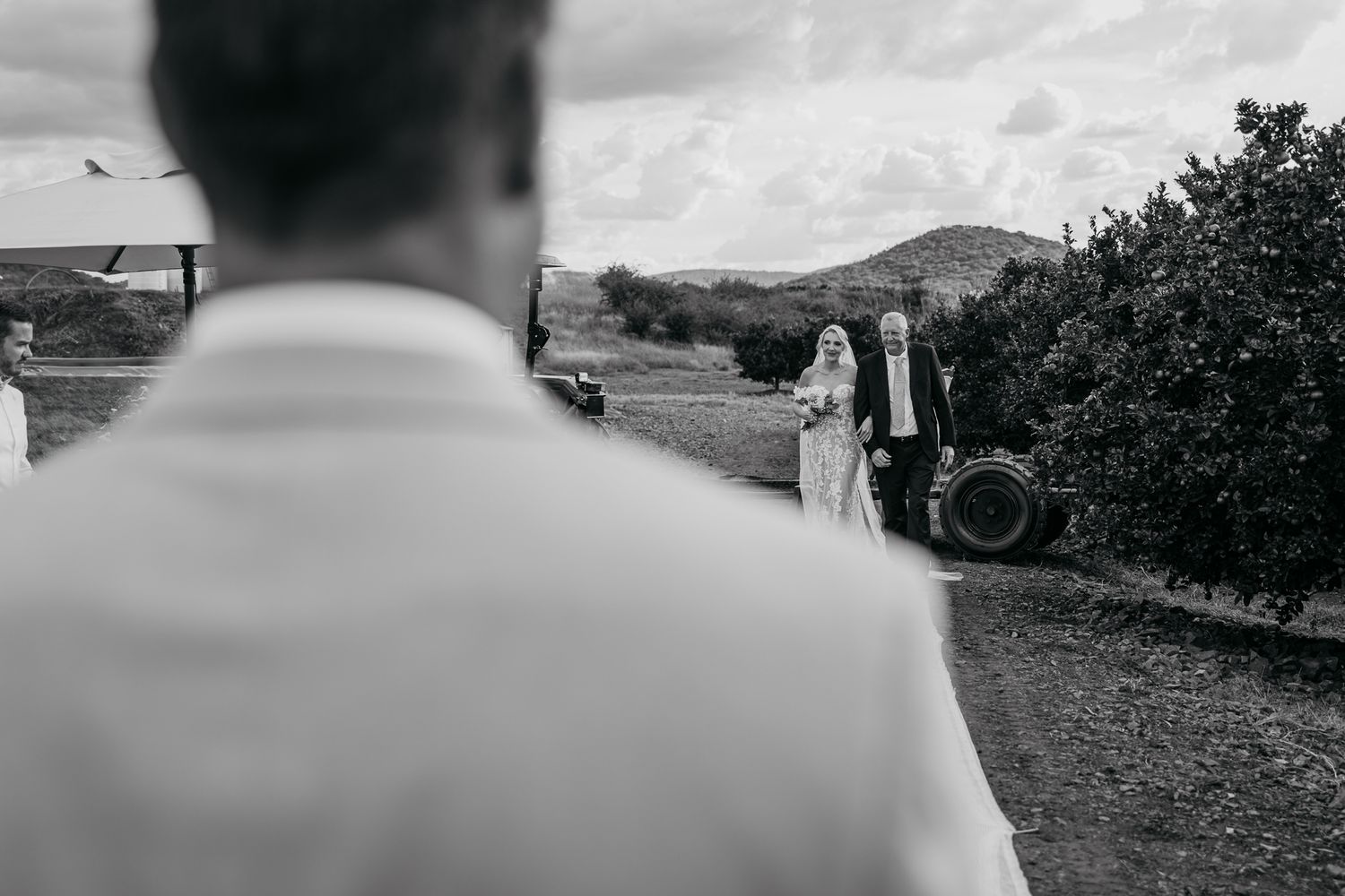 Black and white shot of wedding ceremony from behind guest in rural setting.