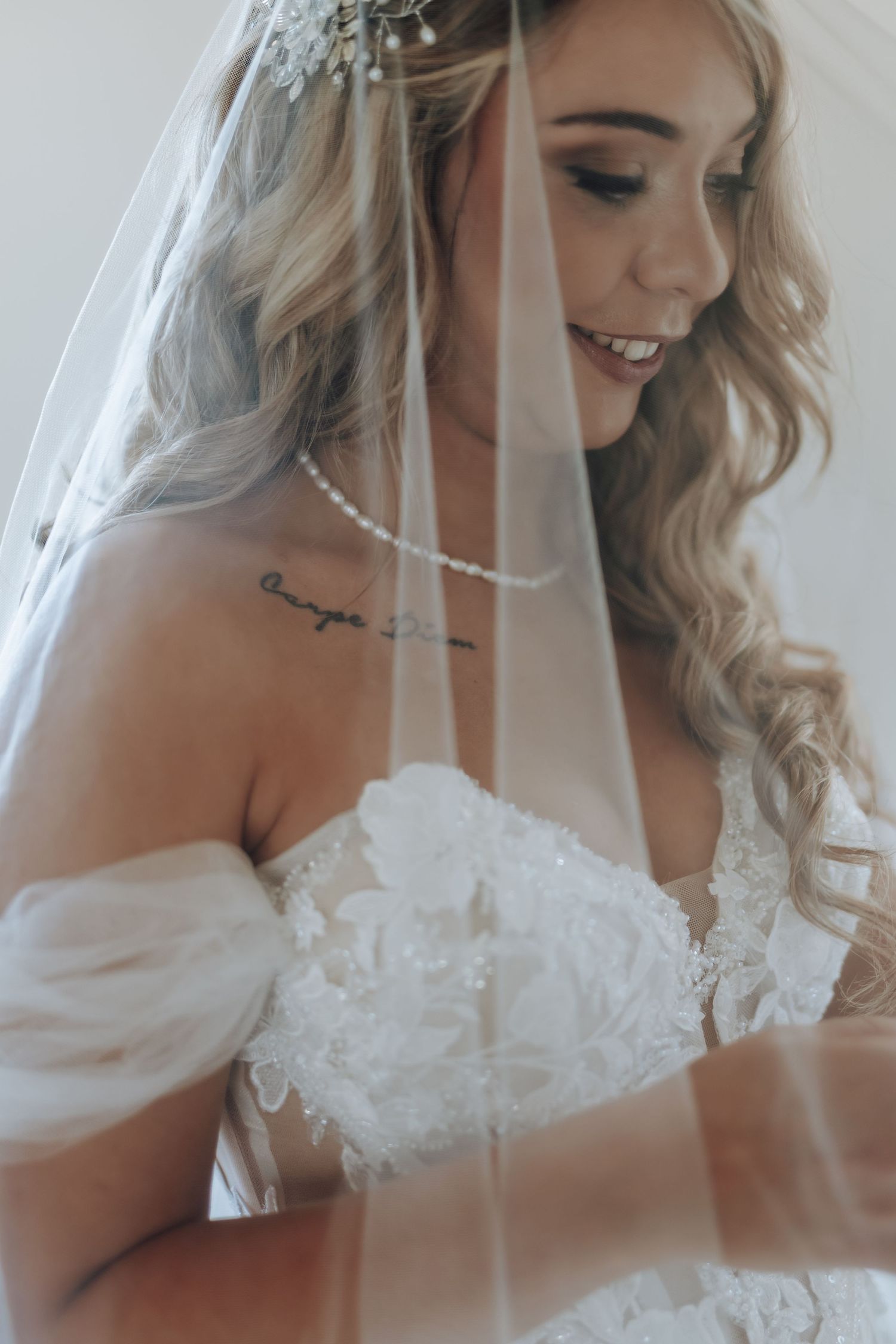 A bride in a white off-shoulder wedding dress with lace details and veil smiles while getting ready.