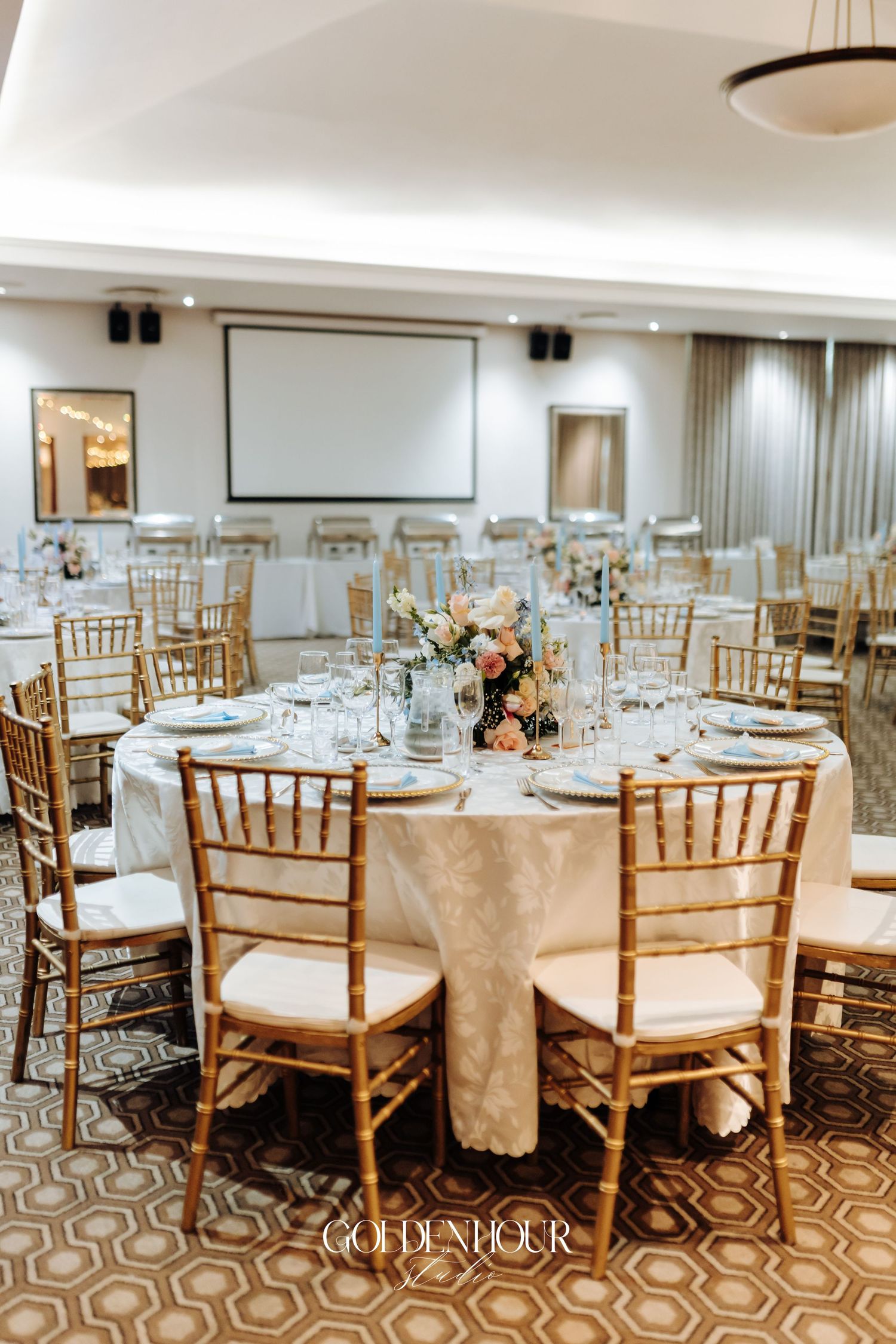 Elegant wedding reception setup with gold chiavari chairs and white tablecloths.
