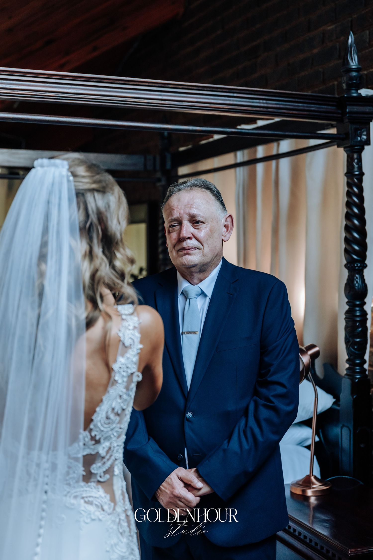 A touching moment at a wedding as a bride in a lace gown stands with someone in a navy suit.