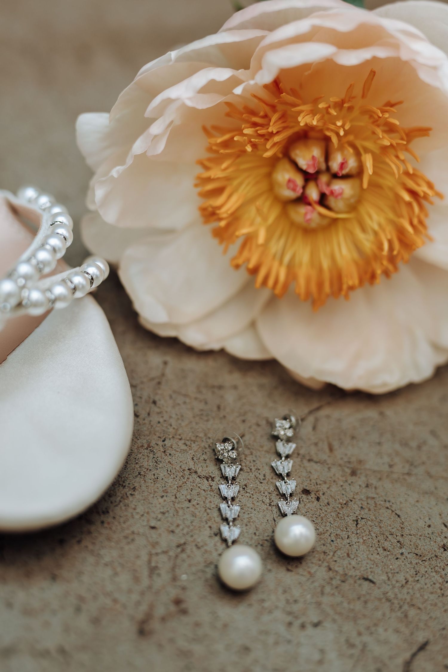 Pearl and crystal bridal jewelry earrings displayed with delicate white and orange flowers on a textured surface.