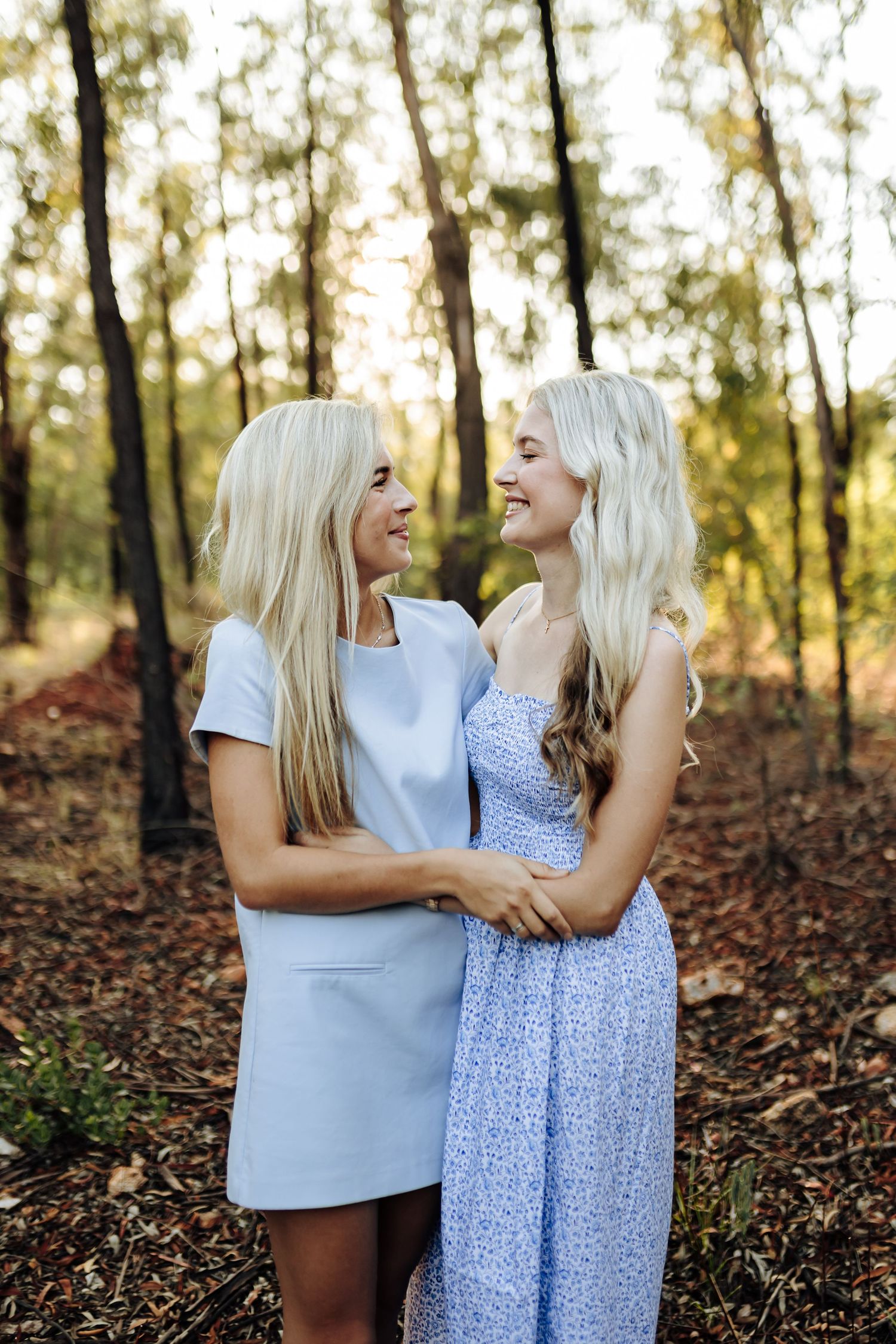 A candid outdoor photography series showing two people in white and blue dresses standing together on fallen autumn leaves.