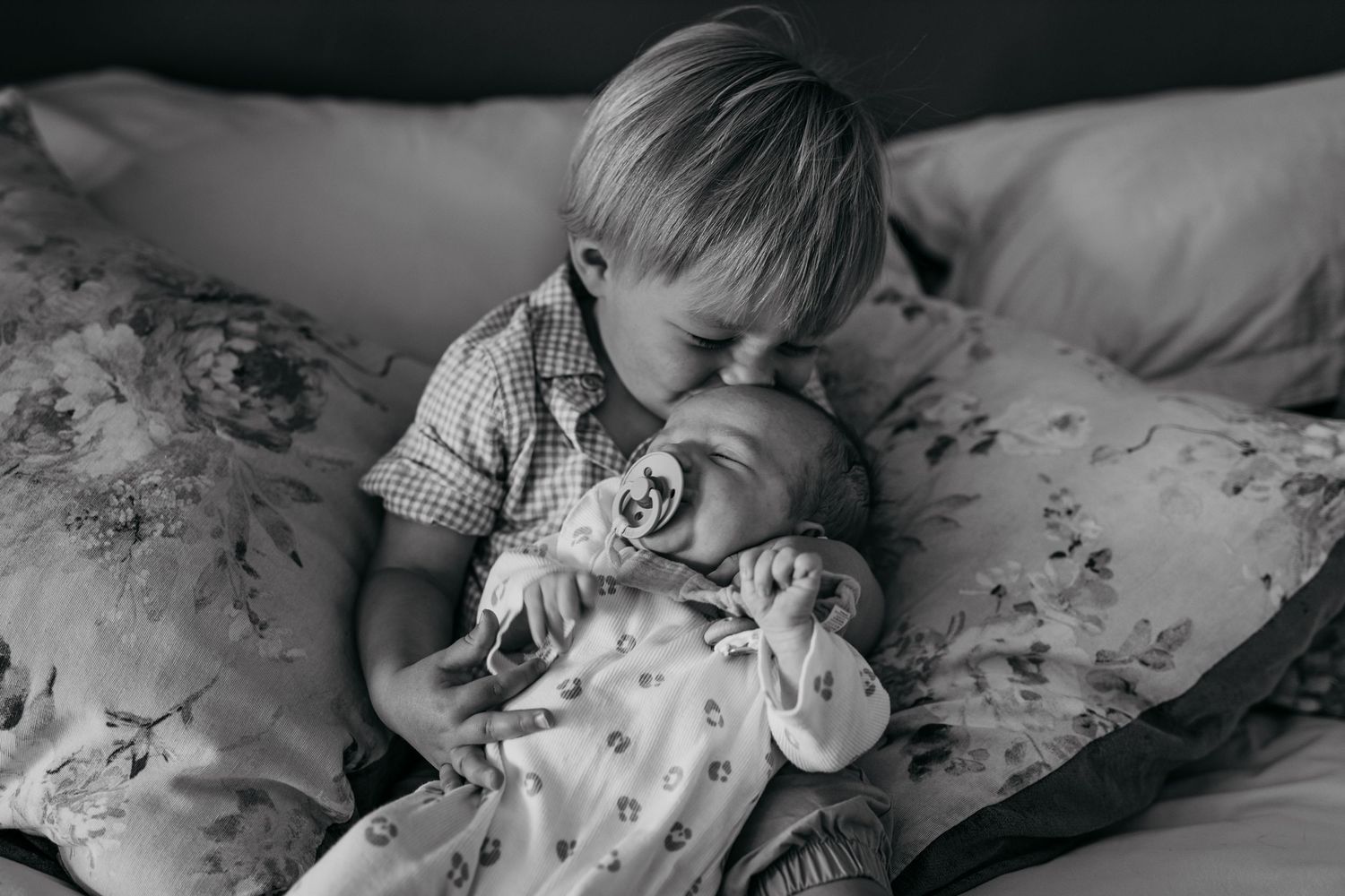 Monochrome image series showing a baby lying on floral bedding, captured from different angles and moments.