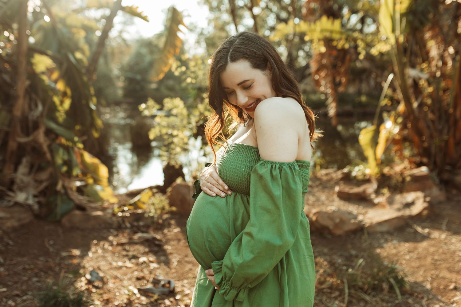 Person wearing an emerald green dress walks through a sunlit autumn forest path, creating a dreamy atmosphere.