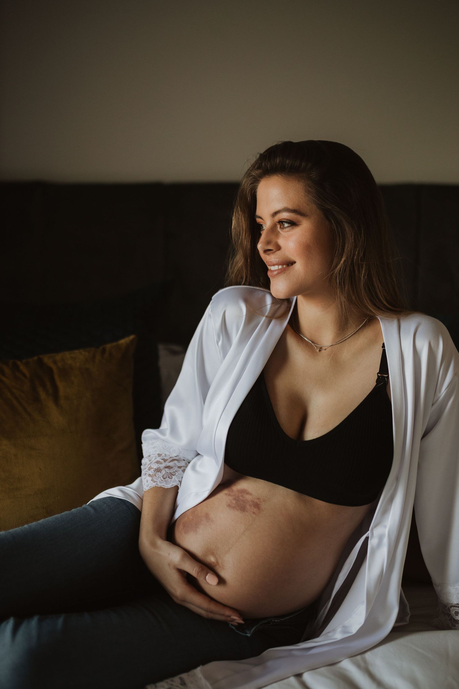 Woman in black clothing and white cardigan poses on couch in moody boudoir photoshoot.