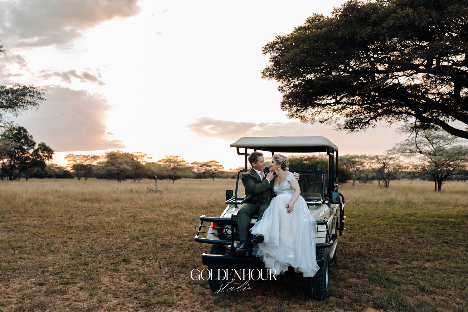 Bride and groom sharing a romantic moment on a safari vehicle at sunset in an open savanna.