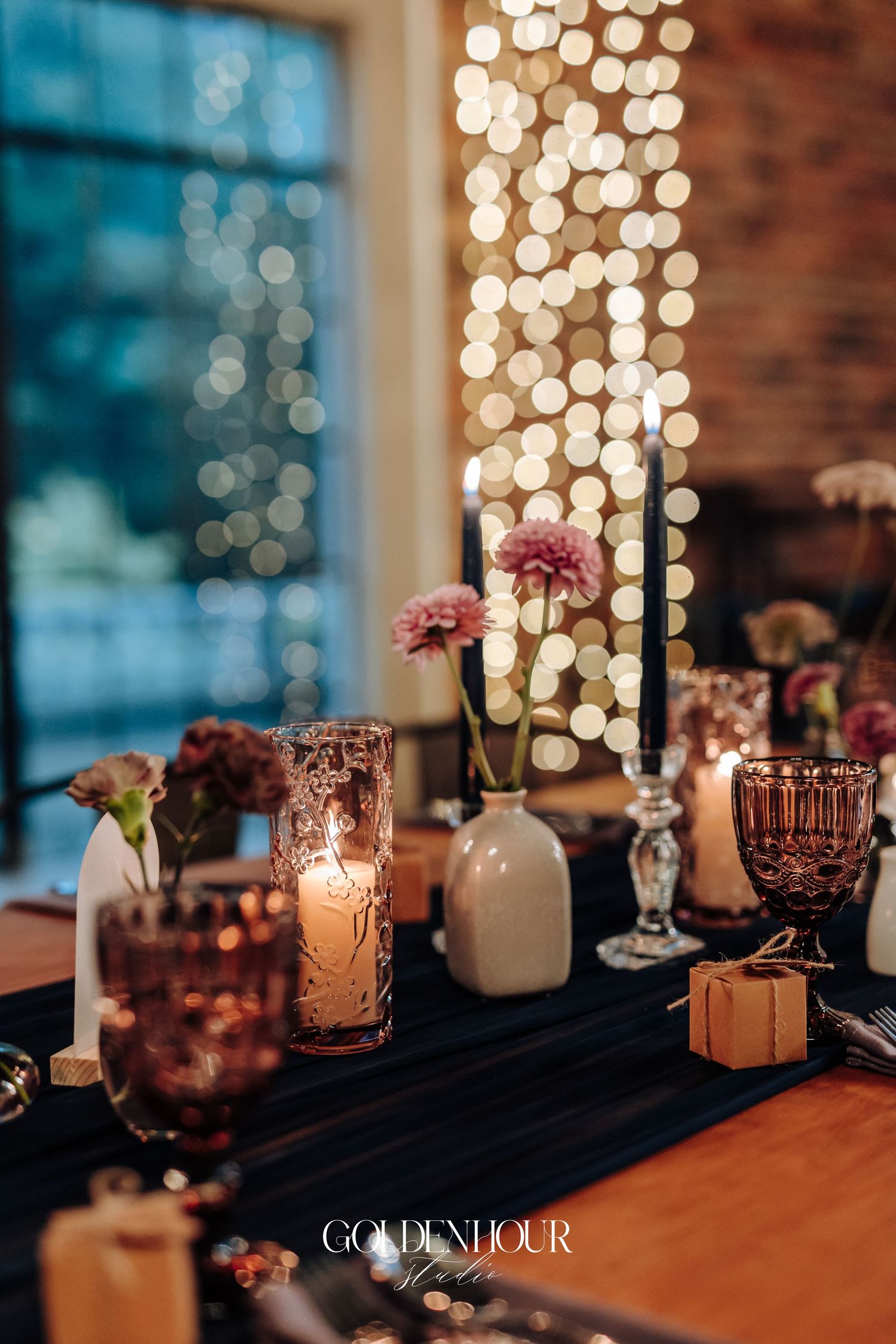 Romantic wedding reception tablescape with candles, pink blooms, and bokeh string lights in background.