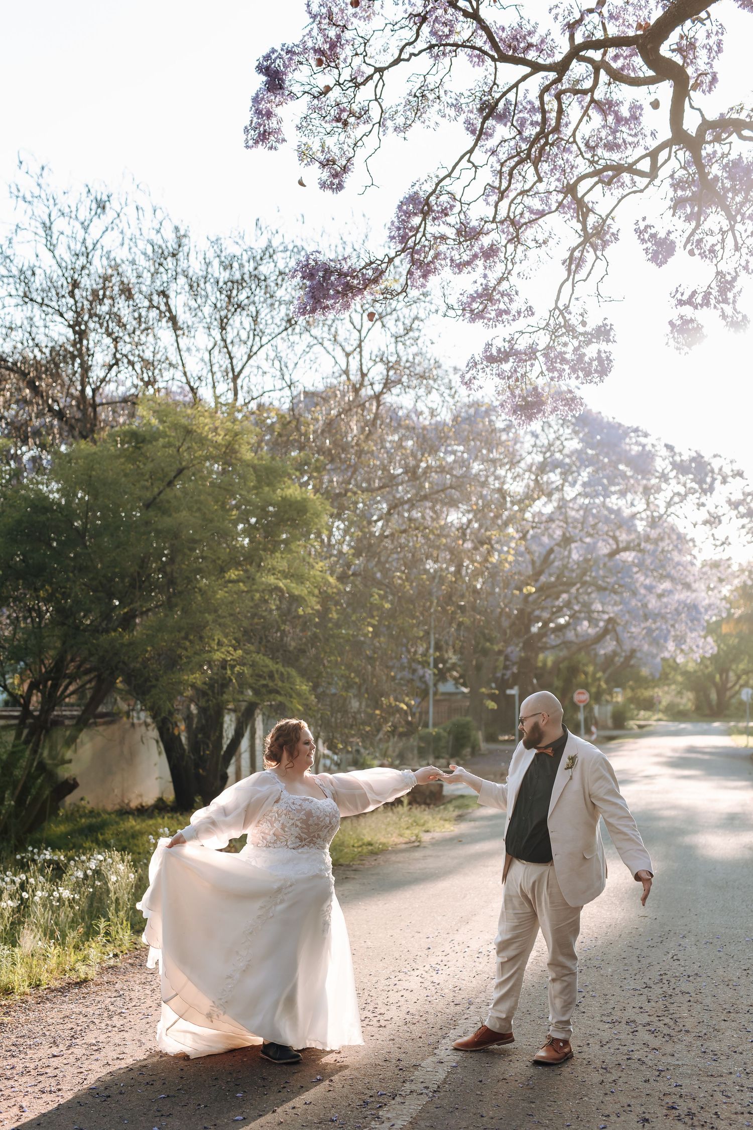 A couple shares a romantic moment on a tree-lined path during a wedding photo session at sunset.