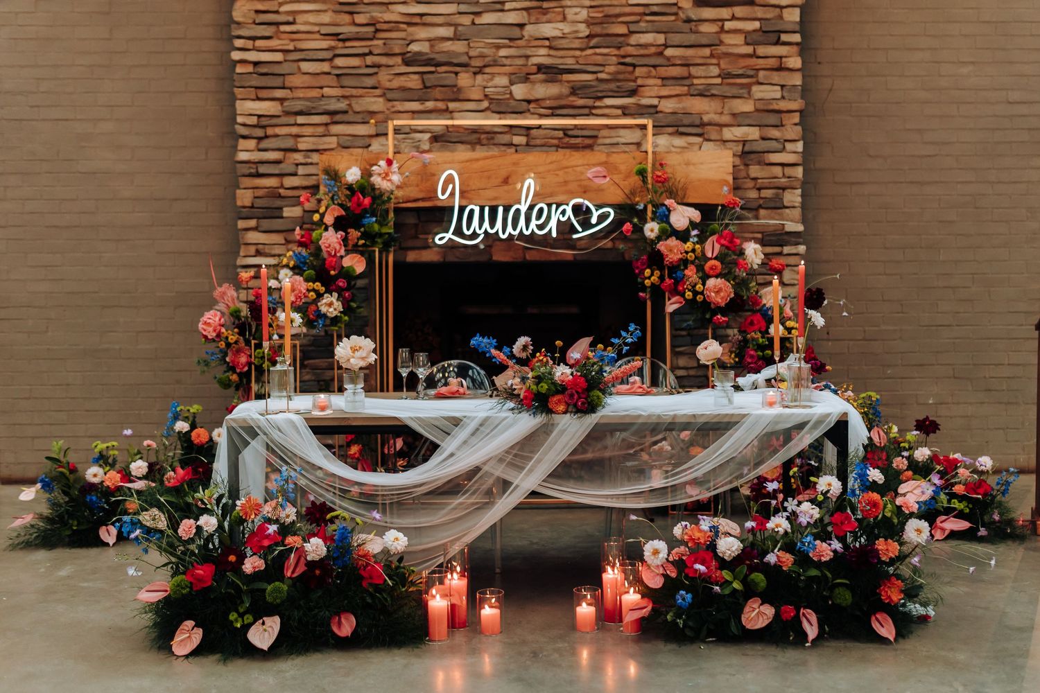A rustic brick wall backdrop with floral arrangements and a white fabric drape for a wedding ceremony setup.