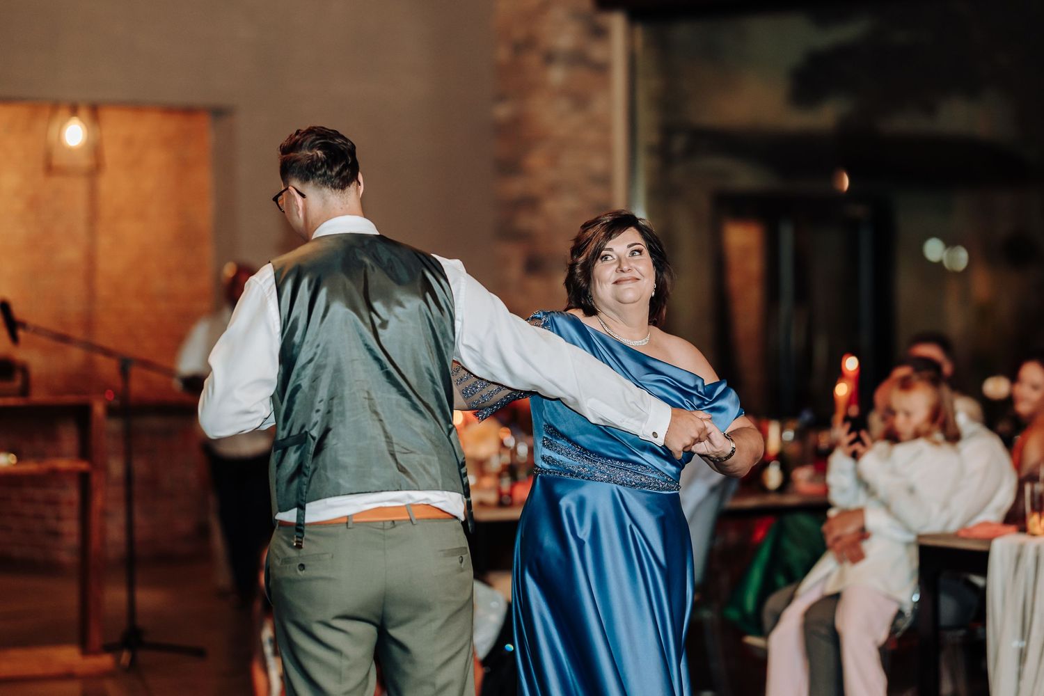 Wedding guests dancing in pairs during an evening reception with warm lighting.