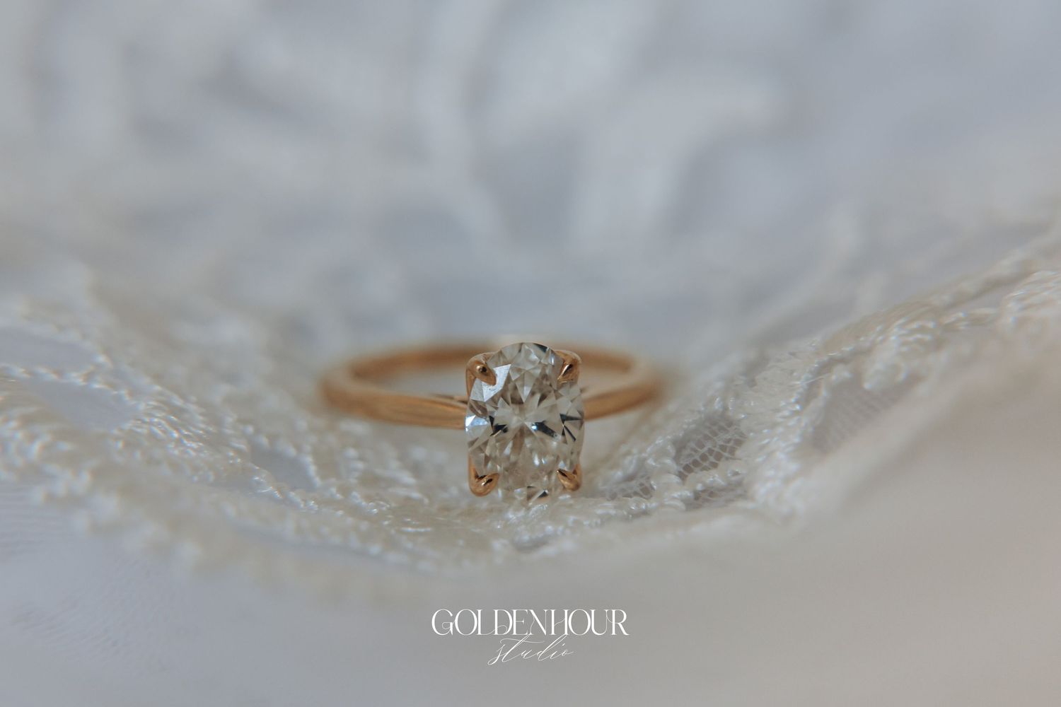 A delicate engagement ring with a round diamond solitaire sparkles against a soft white textured background.