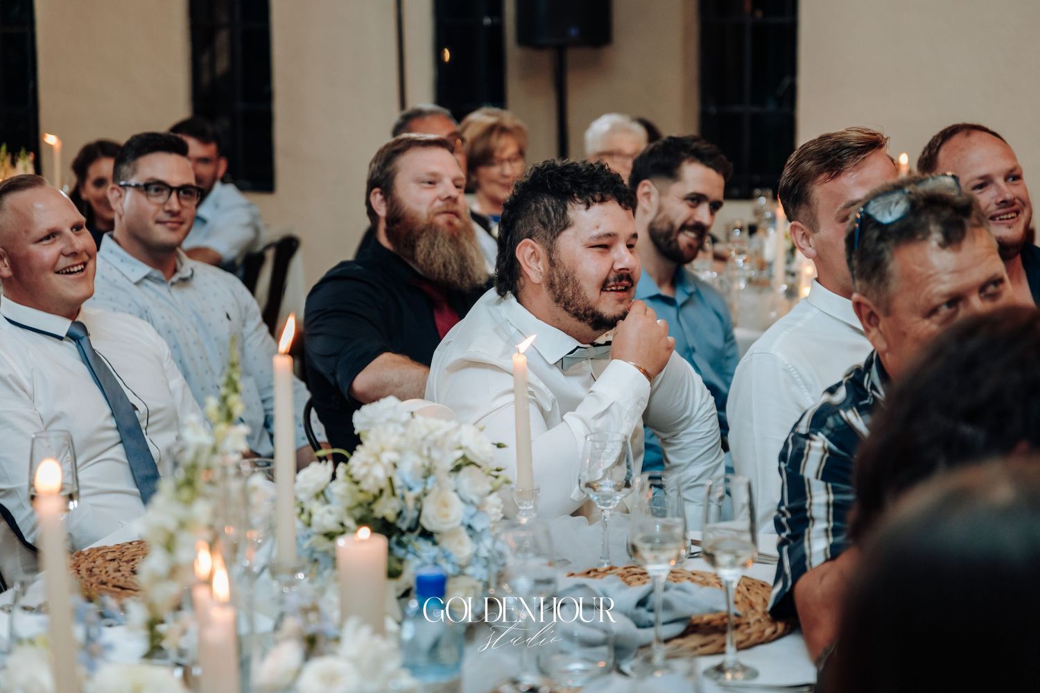 Wedding guests react with joy and laughter during reception speeches at decorated dinner tables.