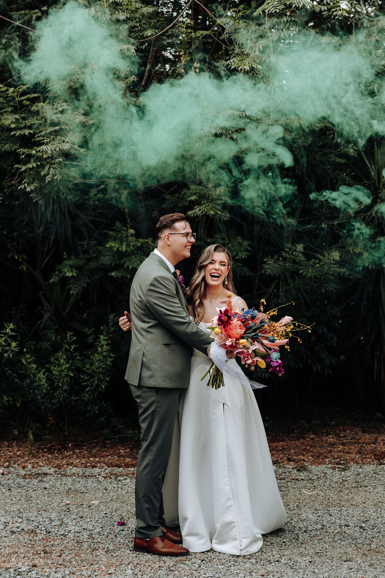 A couple shares a joyful moment with colorful smoke bombs during their outdoor wedding photoshoot.