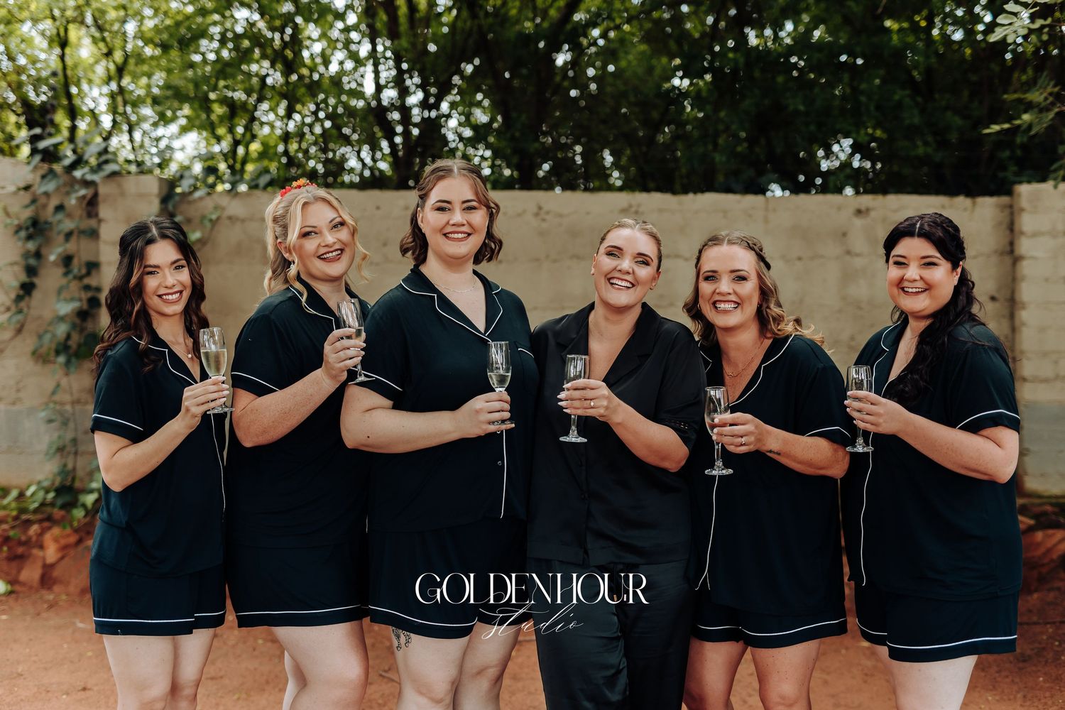 A group of people wearing matching black shirts pose together in an outdoor setting with trees and stone walls.