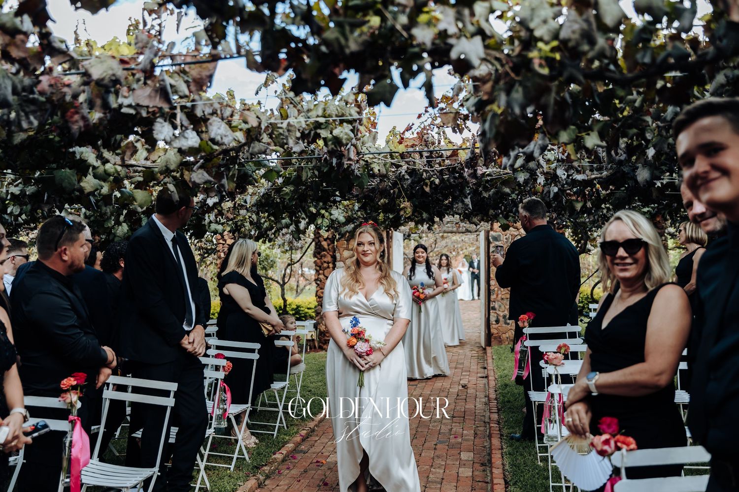 Outdoor garden wedding ceremony under flowering trees with white chairs and floral arch decorations.