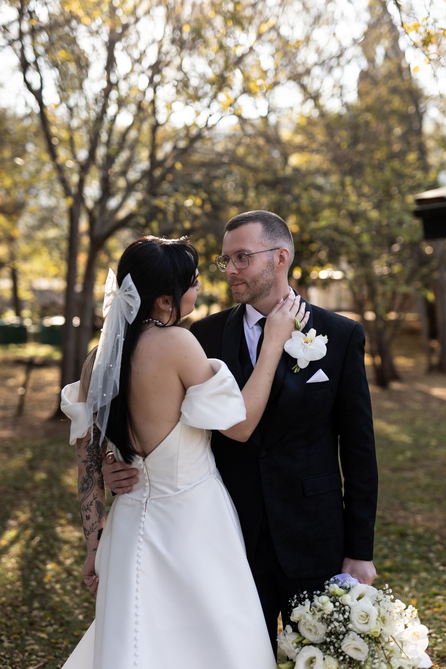 A couple in wedding attire embraces romantically in a fall garden setting with autumn leaves and trees in the background.
